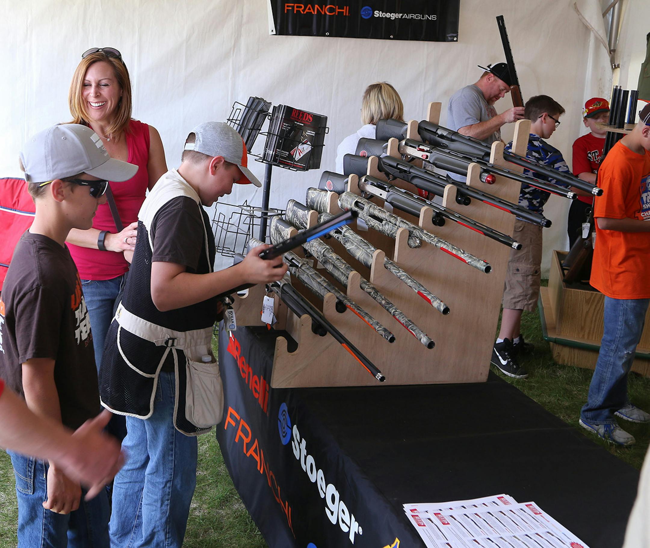 Deb Evans of Lake City, her son Jake, 13, (right) and Jake's friend, Nash Nelson, 13, on Thursday checked out specially designed trapshooting guns at a booth at the state High Shool Trapshooting Championships in Alexandria.