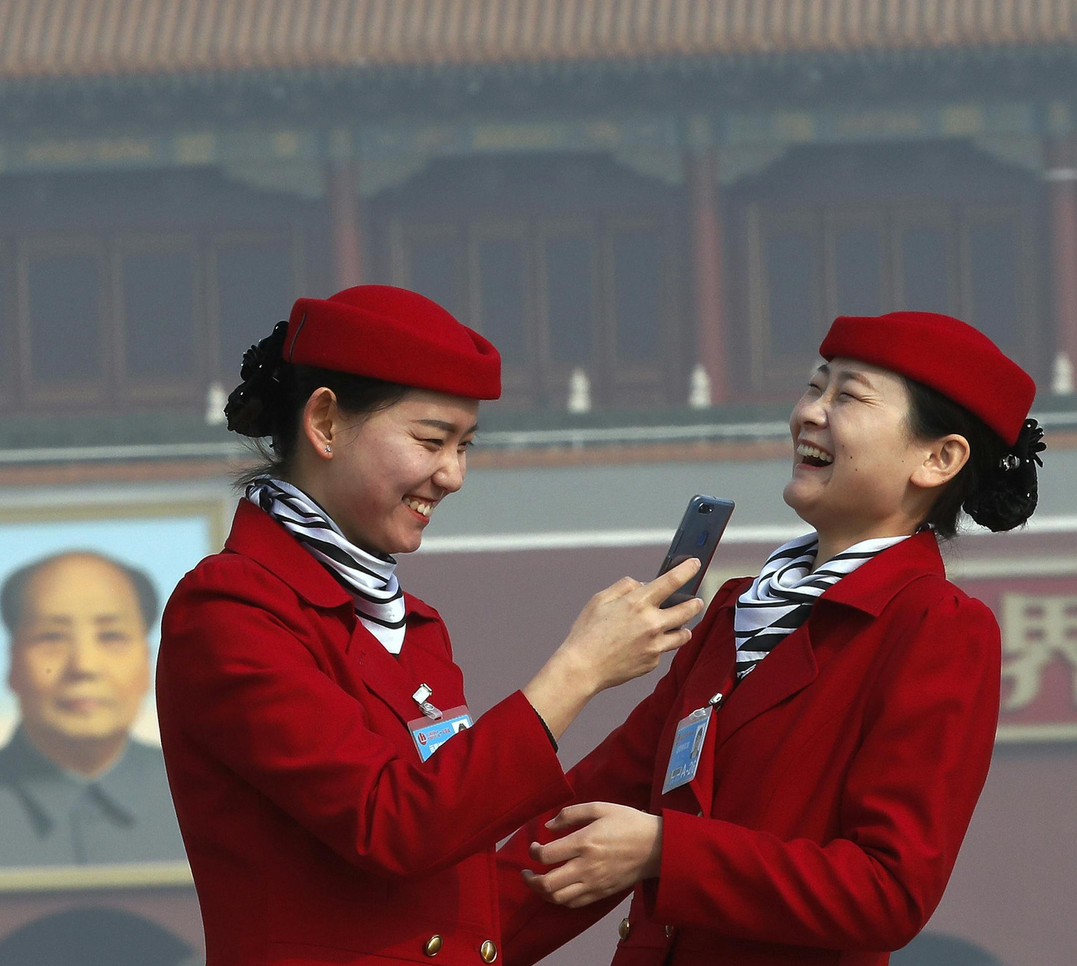 Hospitality staff members have a light moment as they take souvenir pictures on Tiananmen Square during a plenary session of China's National People's Congress (NPC) at the Great Hall of the People in Beijing, Tuesday, March 13, 2018. (AP Photo/Andy Wong)