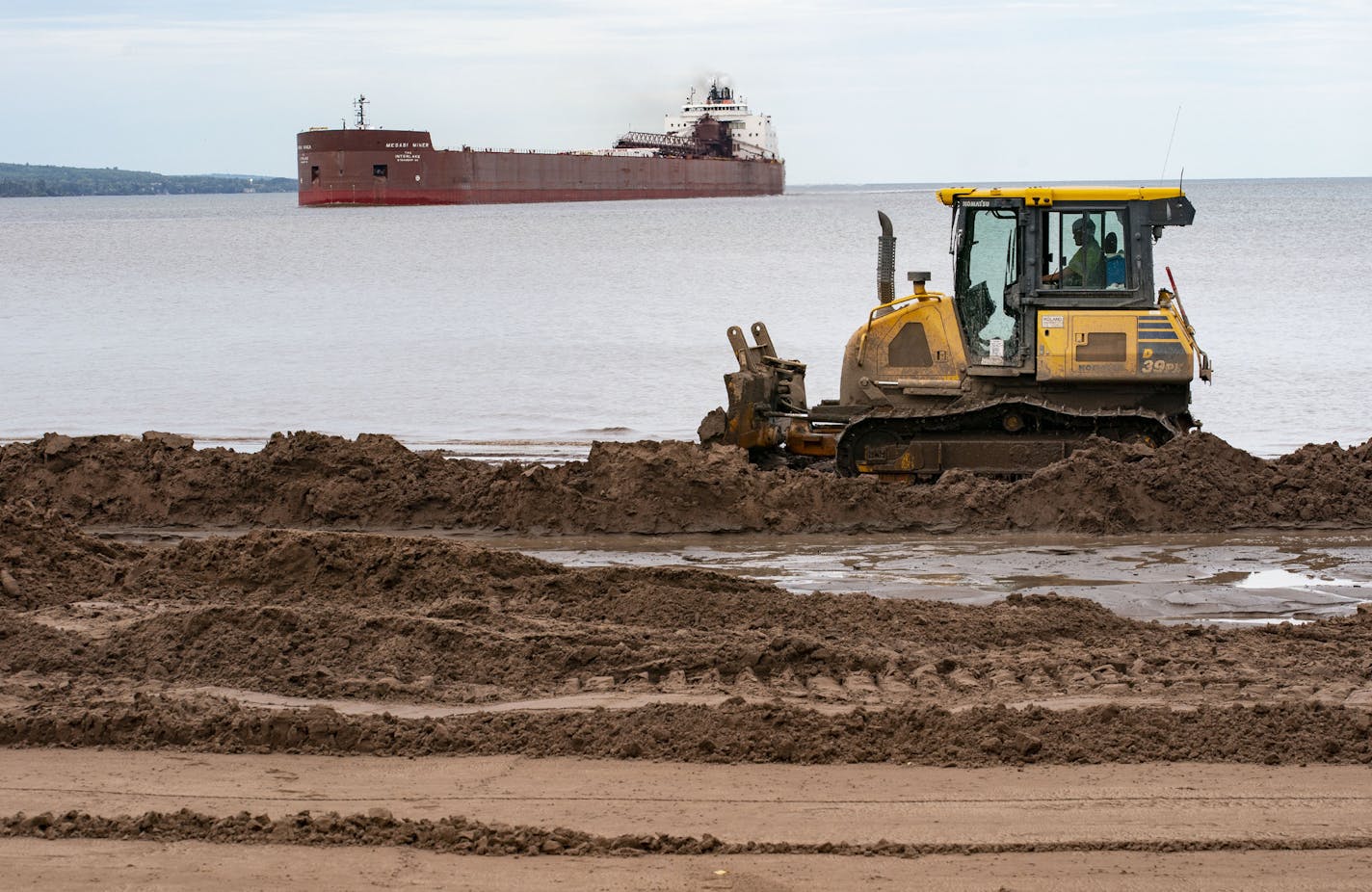 A bulldozer pushed dirt along Park Point beach while the Mesabi Miner pulled into Duluth Harbor on Tuesday afternoon. The bulldozing is part of an effort to raise the beach front and protect homes along the island. ] ALEX KORMANN • alex.kormann@startribune.com Over the past two years the Army Corps of Engineers has dredged up tens of thousands of cubic yards of sludge, silt and sand from the bottom of Duluth Harbor to raise the beach fronts and protect homes along Lake Superior from record high