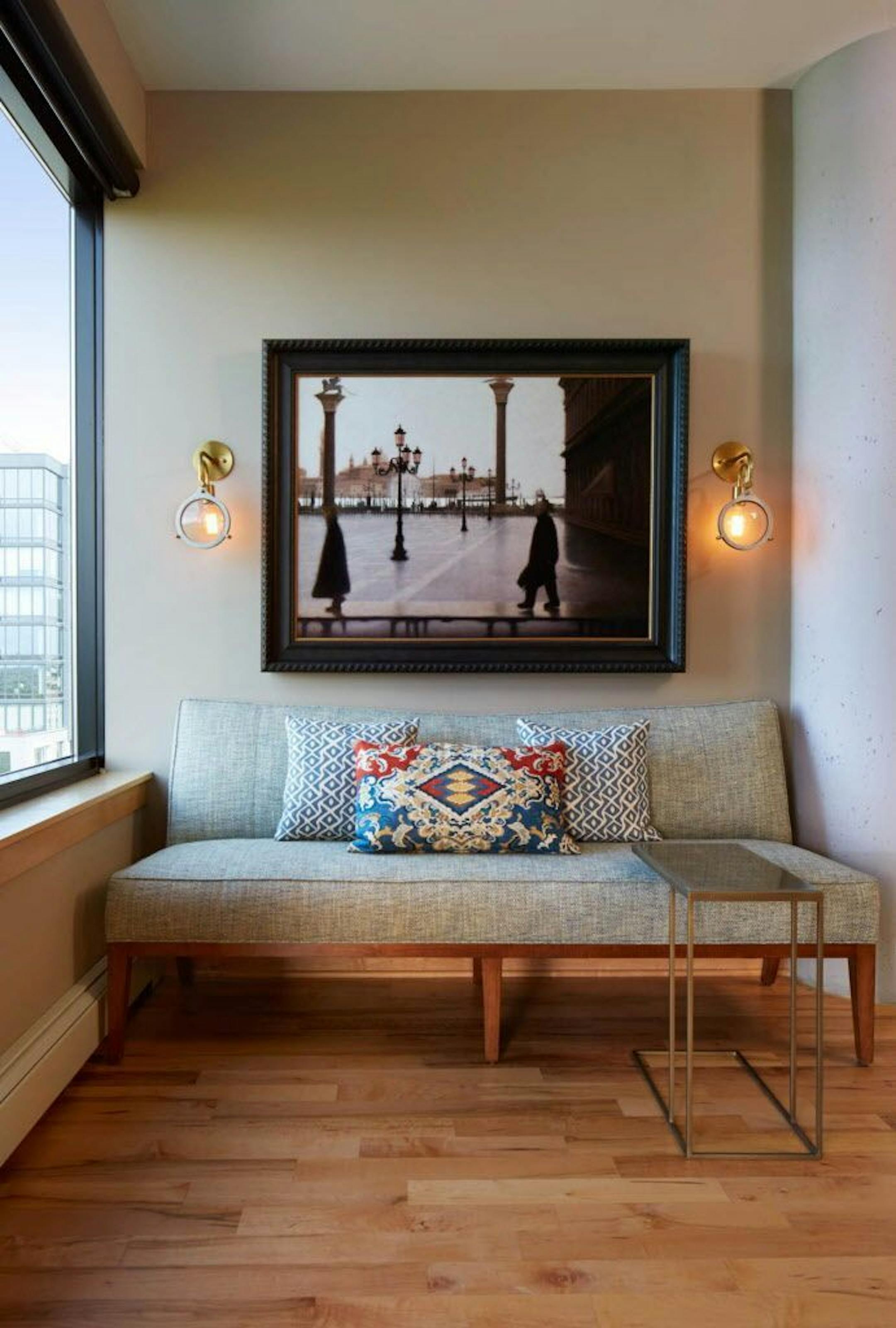 A vignette of a settee under a favorite Rollin Alm oil painting, illuminated by mixed-metal sconces in the art gallery nook..
