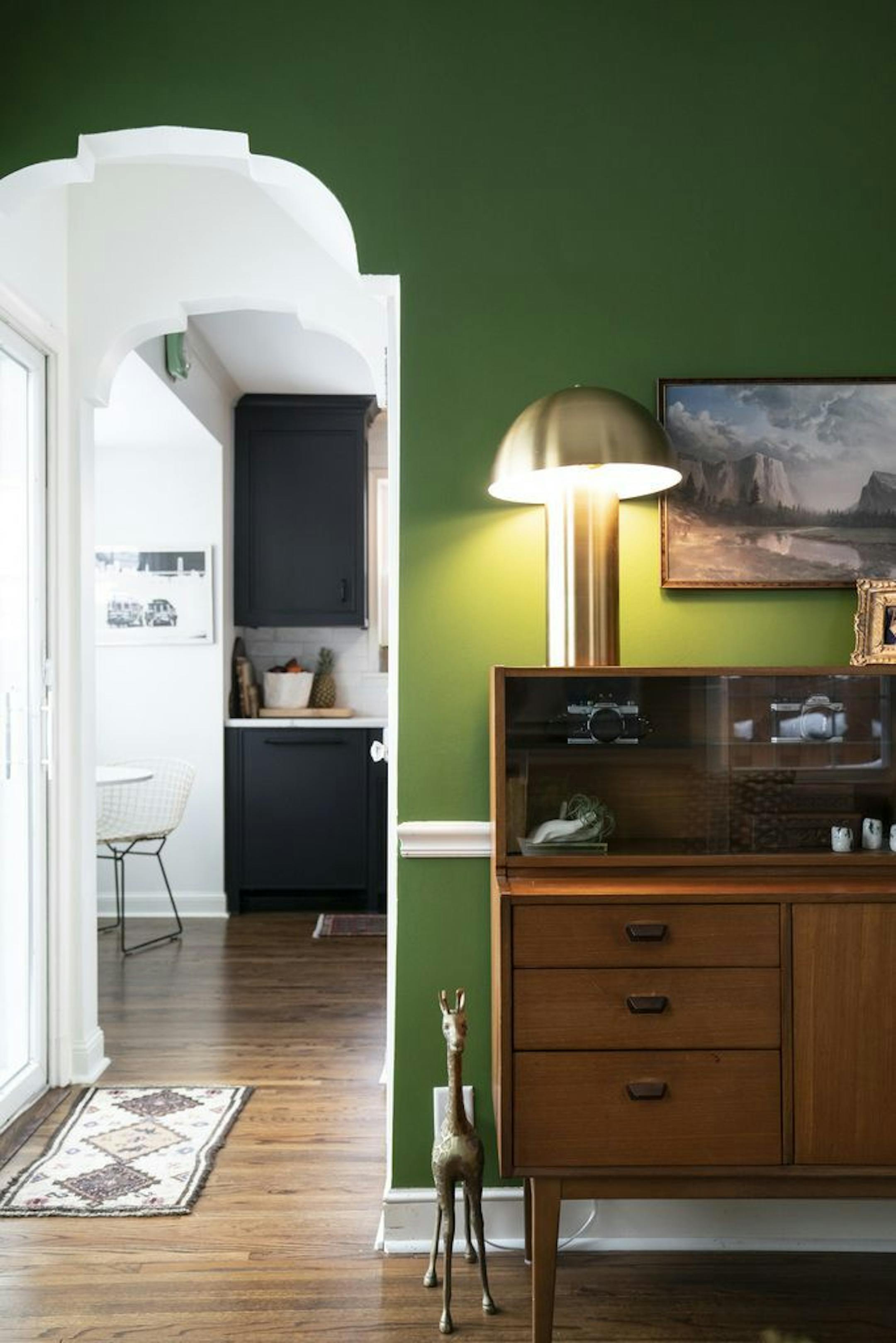 The green sitting room has a white-painted archway leading to the kitchen.