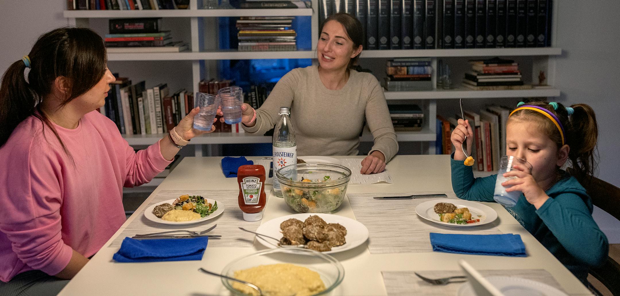 Ukrainian sisters Natalia Kuchma, center, and Yaroslava Kalutska, left, cheer each other as they sit for dinner with Natalia's daughter Solomiia, 5. On this night, they made traditional meatballs and mashed potatoes.