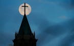 A full moon sets in the morning sky, near dawn, behind the steeple and cross at Lake of the Isles Lutheran Church in Minneapolis in February 2022.