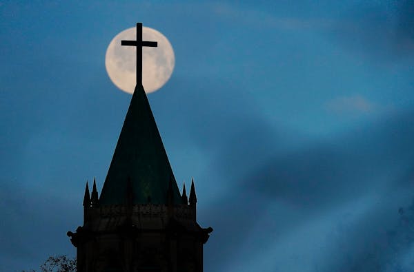 A full moon sets in the morning sky, near dawn, behind the steeple and cross at Lake of the Isles Lutheran Church in Minneapolis in February 2022.