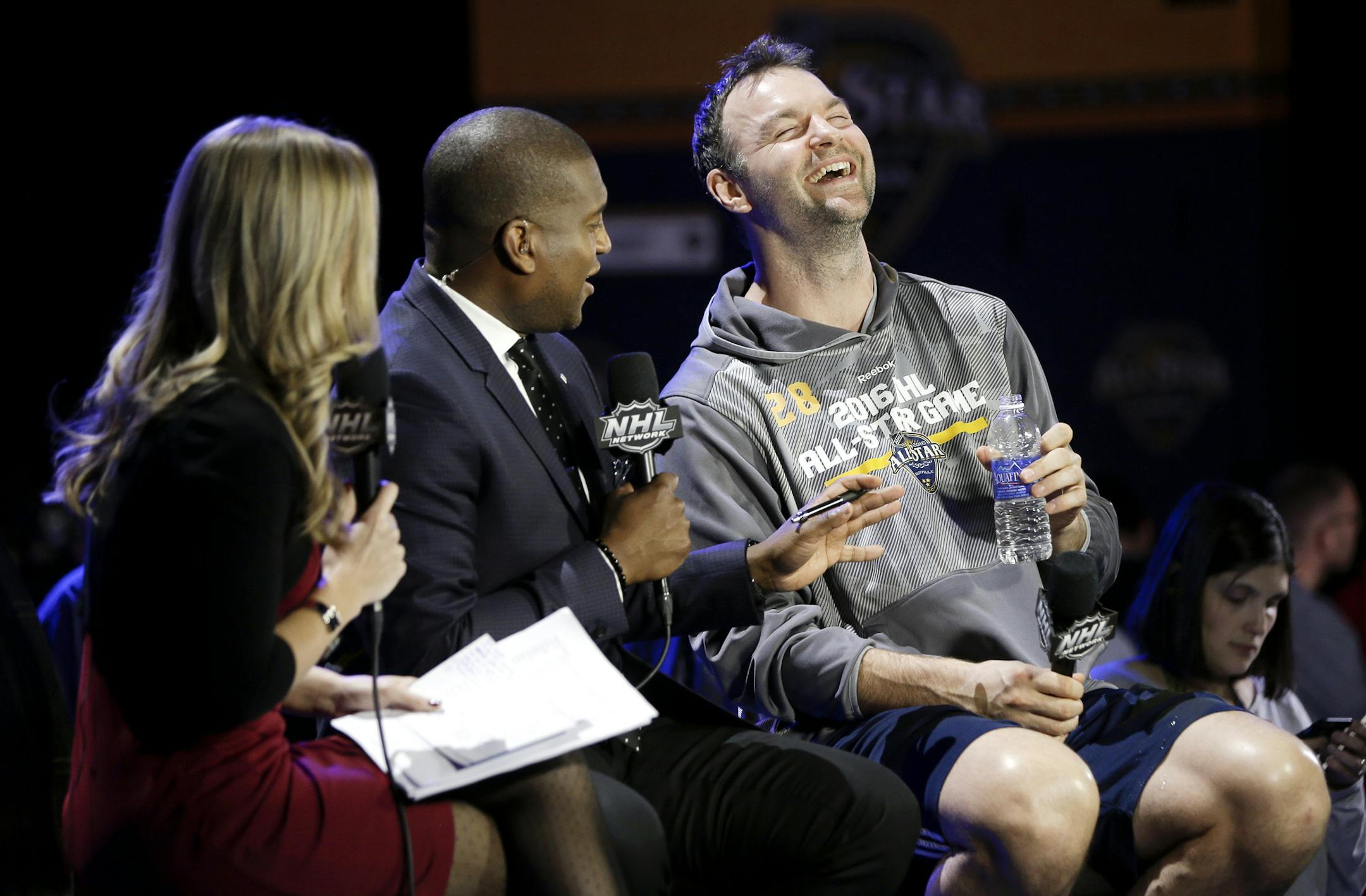 John Scott, right, laughs during a television interview at the NHL hockey All-Star game media day, Friday, Jan. 29, 2016, in Nashville, Tenn. Scott was elected as captain of the Pacific Division, though Arizona traded him to Montreal and he is now at the Canadiens' AHL affiliate in Newfoundland. The game is scheduled to be played Sunday, Jan. 31. (AP Photo/Mark Humphrey)