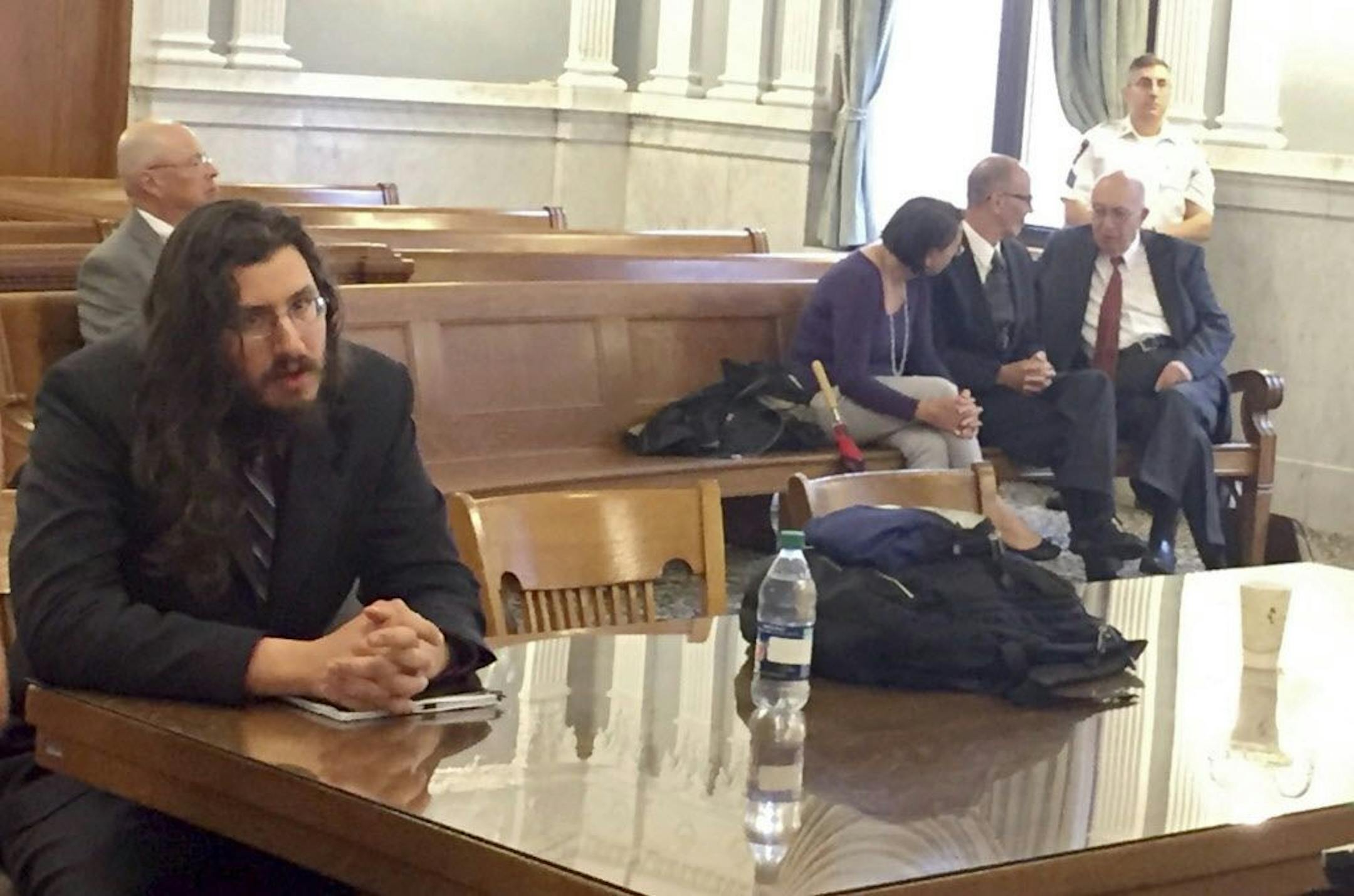 Michael Rotondo, left, sits during an eviction proceeding in Syracuse, N.Y., brought by his parents, Mark and Christina, of Camillus. The two parents confer with their lawyer, Anthony Adorante, in the court gallery behind. Rotondo told the judge Tuesday, May 22, 2018, he knows his parents want him out of their Camillus home, near Syracuse. But he argued he's entitled to six months more time.