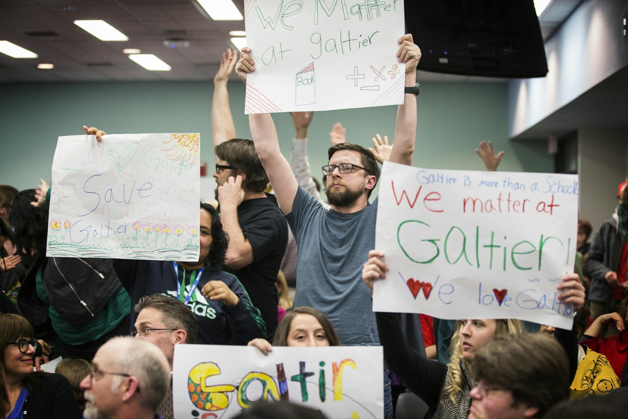 Supporters of Galtier Community School hold up signs during the public comment portion of a St. Paul School Board meeting.