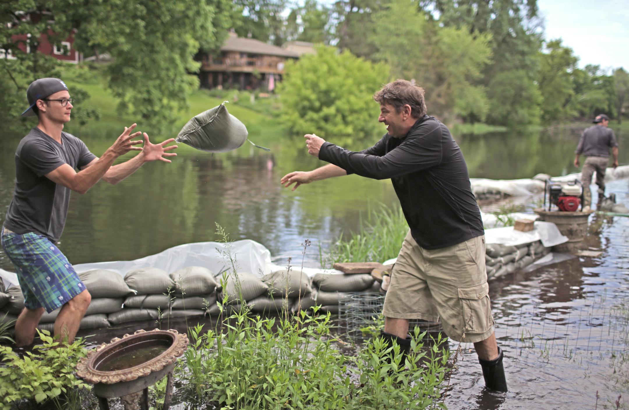 Marshall Rosner, center, tosses a sandbag to Chase Gross in the Gross family backyard on Cascade Lane along Minnehaha Creek Sunday afternoon as neighbor helped neighbor sandbag against the flooded creek. The neighbors had spent the day helping one another sandbag homes on the cul-de-sac. Far in background is neighbor Gary Aulik, also a neighbor. ] David Denney - Star Tribune 6/1/2014 Edina, MN