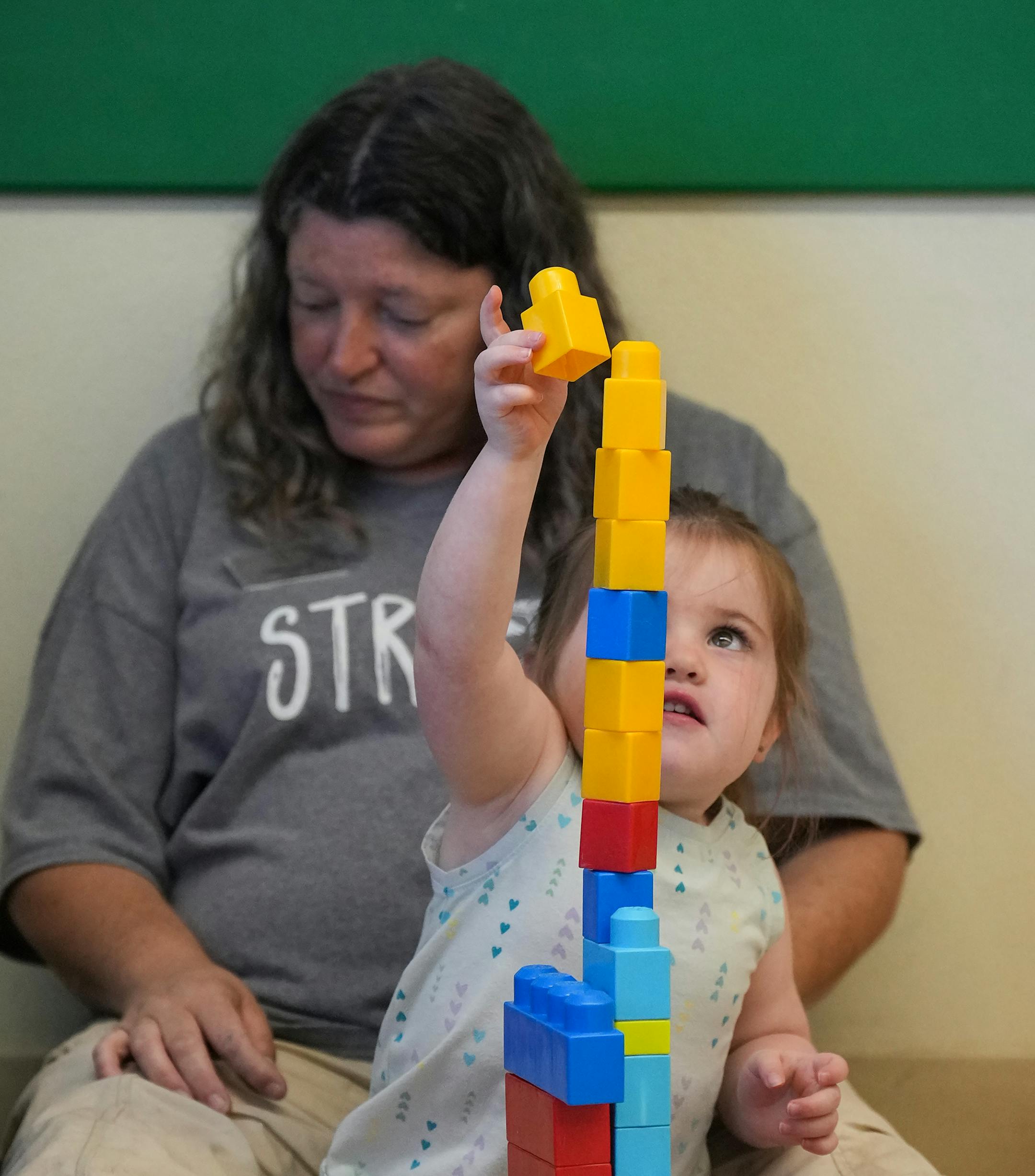 A student works on a block tower while sitting with teacher Idelle Keding on the floor in the class of two-year-olds at Primrose School.