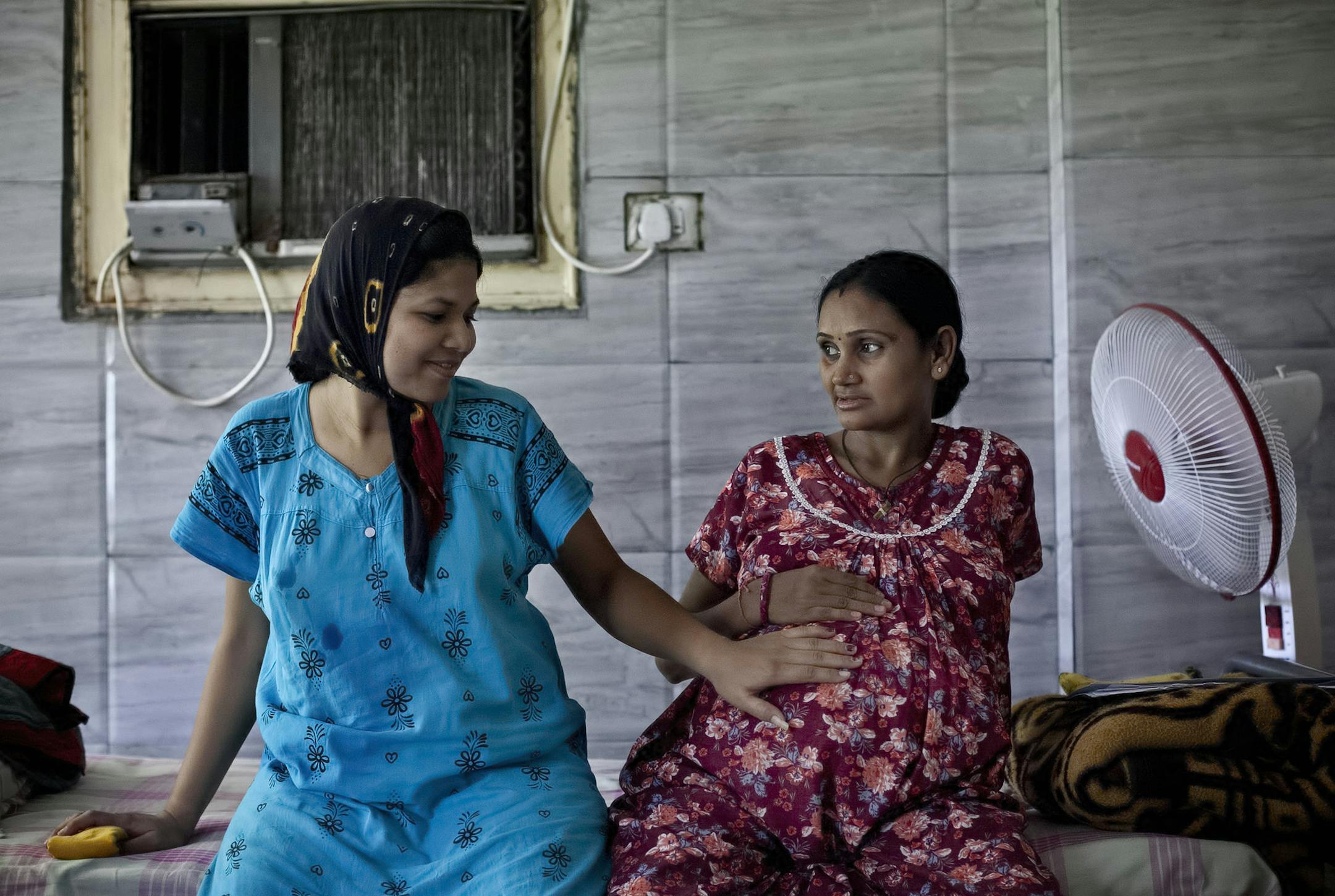 In this Nov. 2, 2015 photo, 30-year-old Bhagwati Chauhan, who gave birth to a Canadian couple's child on Oct. 27, touches the 9-month pregnant belly of 35-year-old Chandrika Makwana, who is carrying twins for an American couple, at the Akanksha Clinic, one of the most organized clinics in the surrogacy business, in Anand, India. Chauhan, whose husband died recently, plans to use the money she will earn as a surrogate to buy a house and send her son to school. The Indian government recently banne