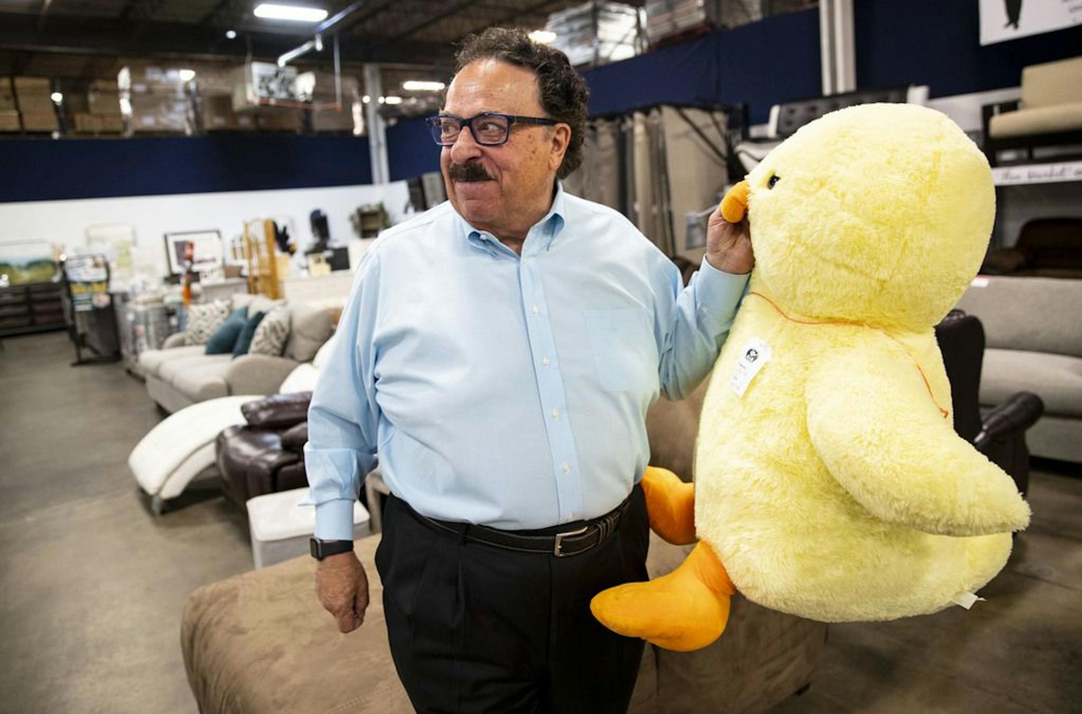 Dick Enrico held up a large plush duck while telling a story about how he offered to sell a man a couch for $35 if he bought the duck. The man later returned the duck and kept the couch.