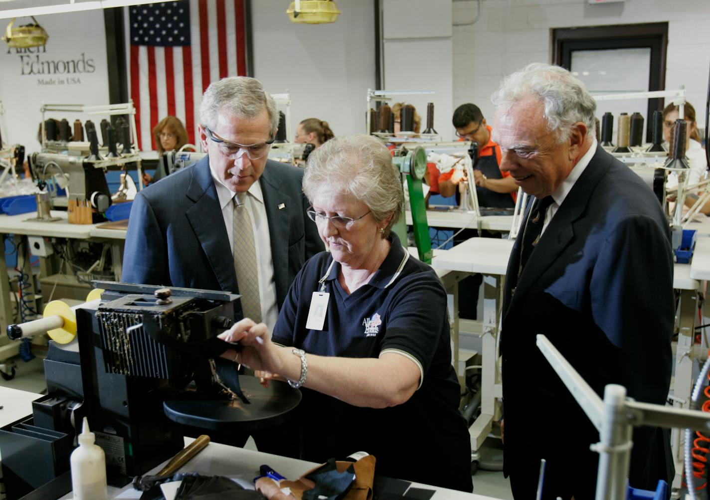 President George W. Bush observes sewer Eileen Staege, at Allen Edmonds Shoe Bank as John Stollenwerk, the company's chief executive officer looks on at right, in Port Washington, Wisconsin, Tuesday, July 11, 2006. Photographer: Karen Sherlock/POOL via Bloomberg News