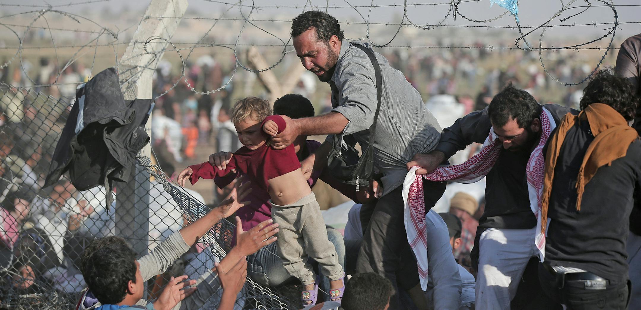 FILE - In this Sunday, June 14, 2015 file photo, a Syrian refugee carries a baby over the broken border fence into Turkey after breaking the border fence and crossing from Syria in Akcakale, Sanliurfa province, southeastern Turkey. A Kurdish official says a new administration has been formed for a majority Sunni-Arab town controlled by Syrian Kurds, expanding the ethnic groupís semi-autonomous administration in northern Syria. (AP Photo/Lefteris Pitarakis, File) ORG XMIT: MIN201511051917372
