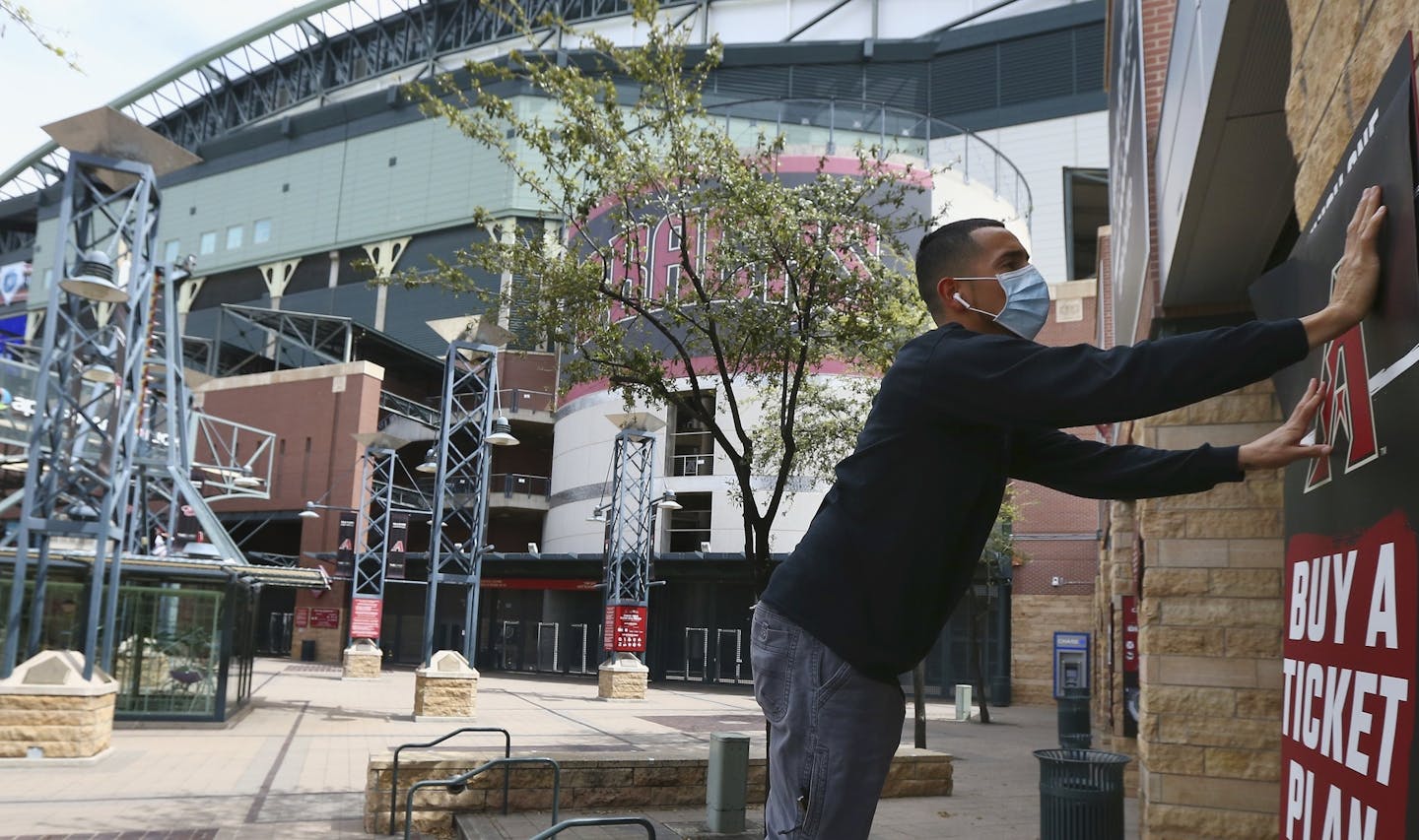 Joey Rodriguez, of Image Craft, installs an advertising banner in front of Chase Field Thursday, March 26, 2020, in Phoenix. The Arizona Diamondbacks would have hosted the Atlanta Braves in their season-opening baseball game Thursday, but the start of the MLB regular season is indefinitely on hold because of the coronavirus pandemic. (AP Photo/Ross D. Franklin) ORG XMIT: AZRF104