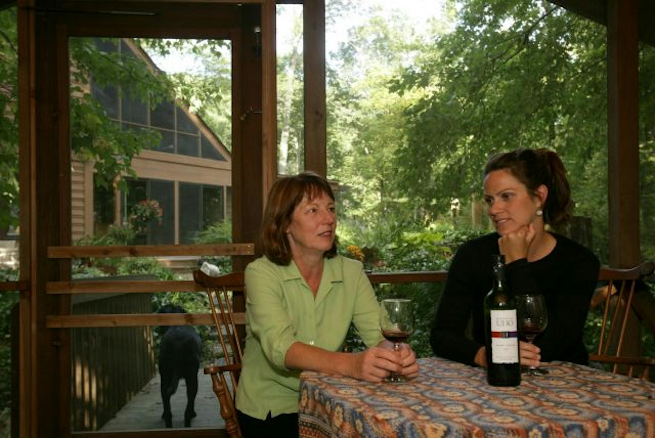 Lori Gordon, left, and her tenant/new friend Brooke Thalacker shared conversation and wine on Gordon's porch on an early fall evening. Their dogs, Ruby (Thalacker's black Labrador retriever) and Steve (Gordon's white poodle cross), also enjoy each other's company.