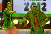 Justin Bieber stands to the left of Will Smith and points off-camera. The two men are drenched in a green slimy liquid.