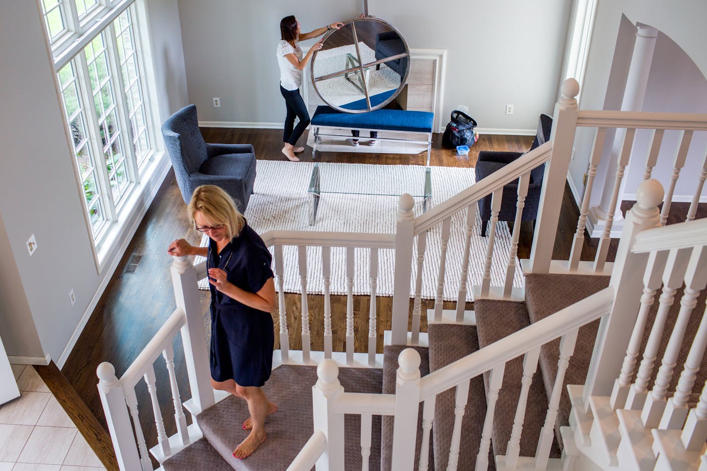 Showhomes franchise owner Karen Galler stands on the stairs while Sondra Bambery waits to place the mirror above the fireplace inside the Eden Prairie house they are staging. ] COURTNEY PEDROZA &#x2022; courtney.pedroza@startribune.com; Showhomes franchise owner Karen Galler is a house stager; Thursday 08/10/2017; Eden Prairie., MN