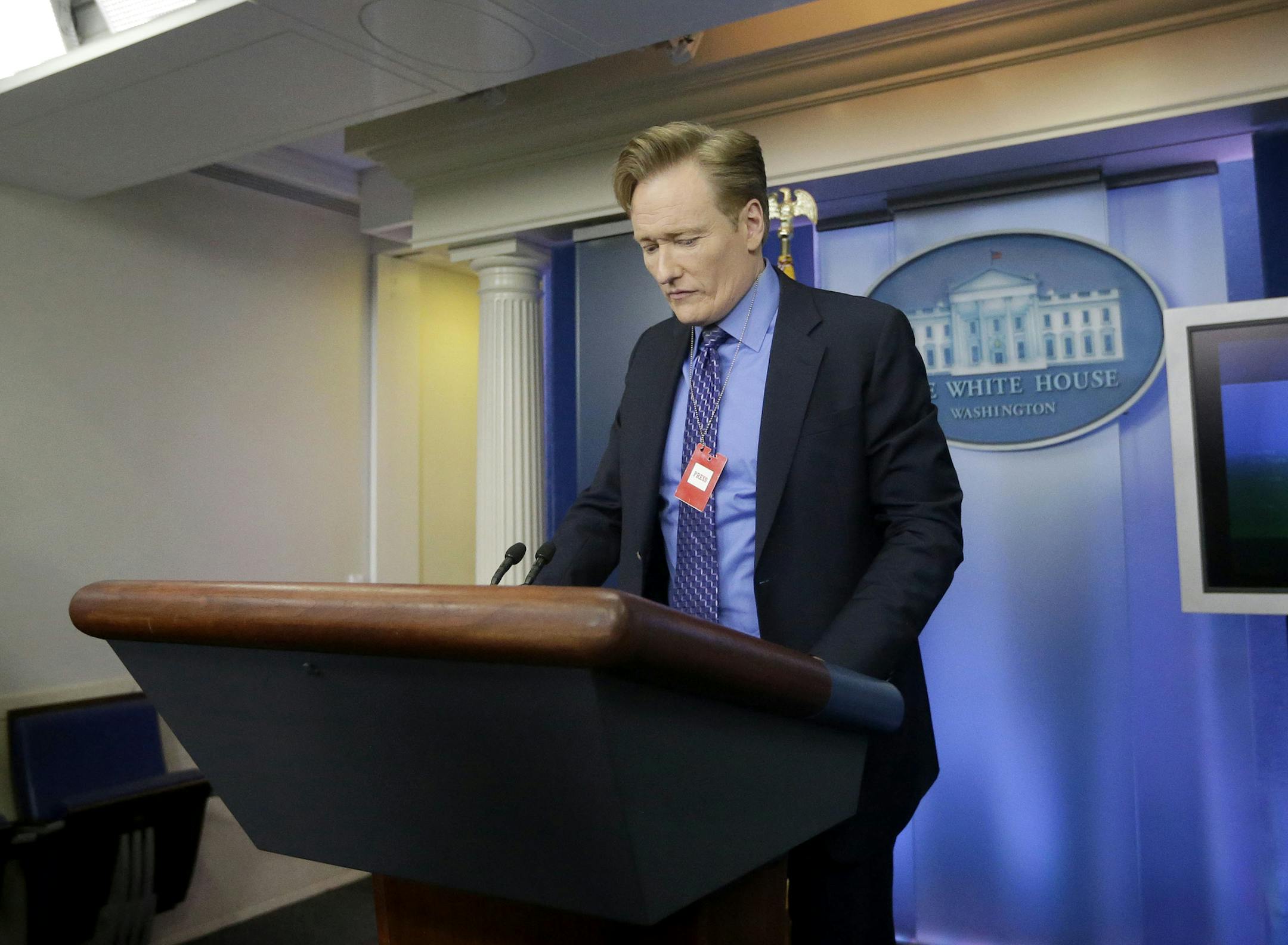 Late-night television host and comedian Conan O'Brien stands behind the podium as he tours the Brady Press Briefing room of the White House in Washington, Friday, April, 26, 2013. O'Brien visited the White House ahead of his schedule hosting of the annual White House Correspondents Dinner on Saturday. (AP Photo/Pablo Martinez Monsivais)