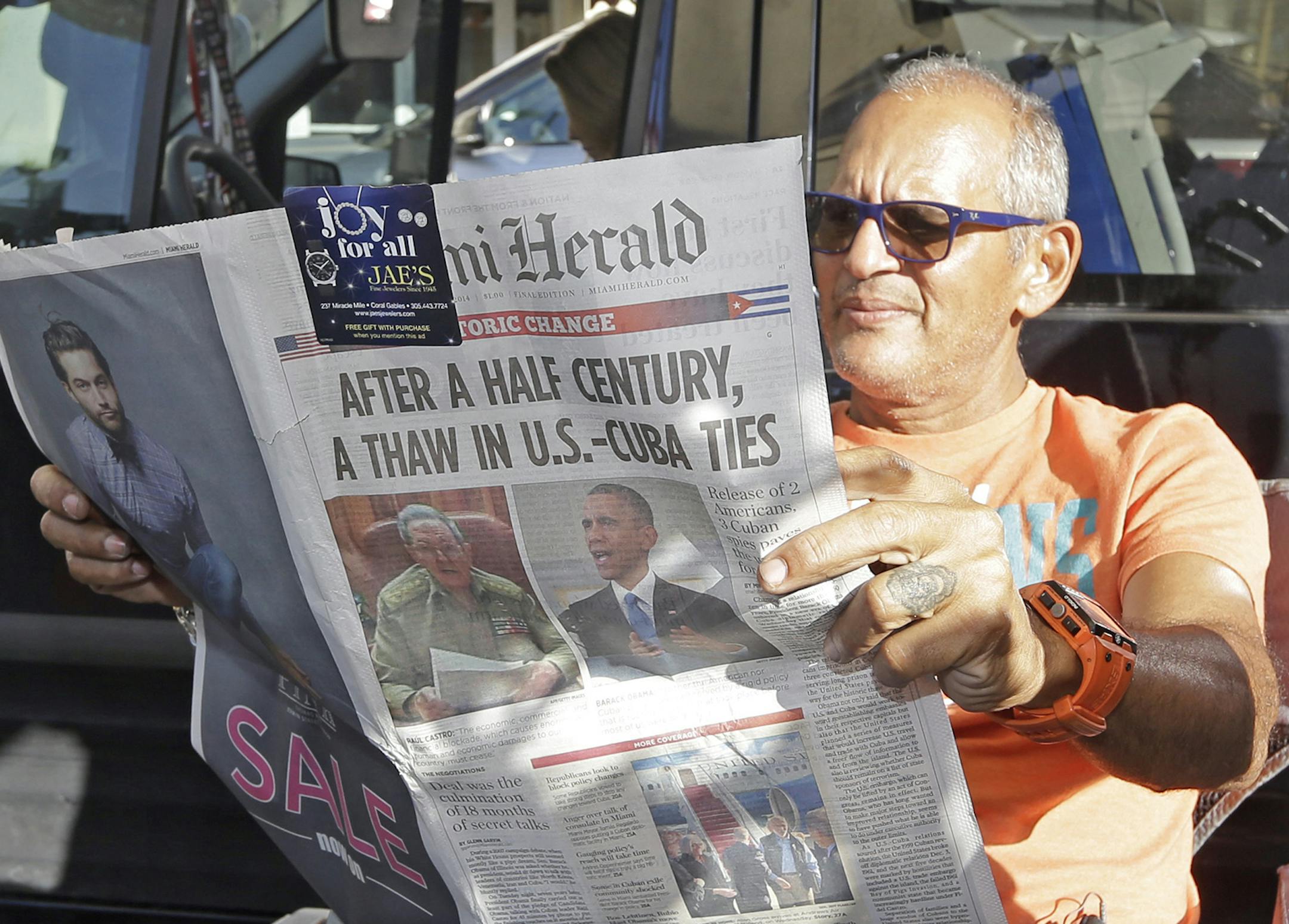 MSNBC photographer Tony Zumbado reads the Miami Herald in the Little Havana area of Miami, Thursday, Dec. 18, 2014, as news agencies from all over the world prepare to cover the reaction of the Cuban-Americans to the surprising move by President Barack Obama to restore the nation's ties with Cuba. The U.S. and Cuba will begin taking steps to restore full diplomatic relations, marking the most significant shift in U.S. policy toward the communist island in more than half a century. (AP Photo/Alan