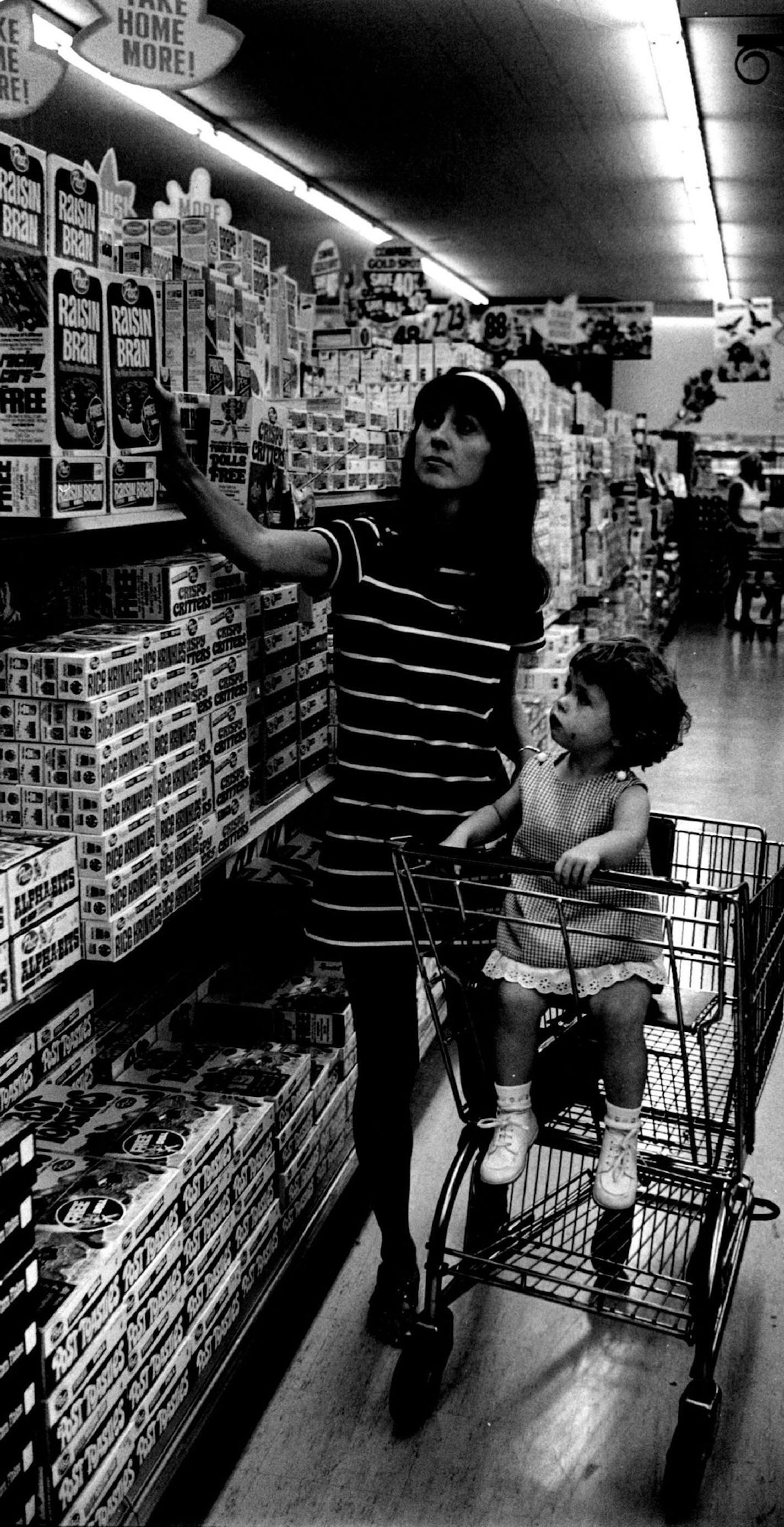 July 30, 1970 Mrs. Wilfried Volk reached for a box of cereal as her 2-year-old daughter Cassandra - "the only cereal eater in the family" - looked on. Mrs. Volk said she will continue to buy Sugar Crisp for Cassandra. Donald Black, Minneapolis Star Tribune