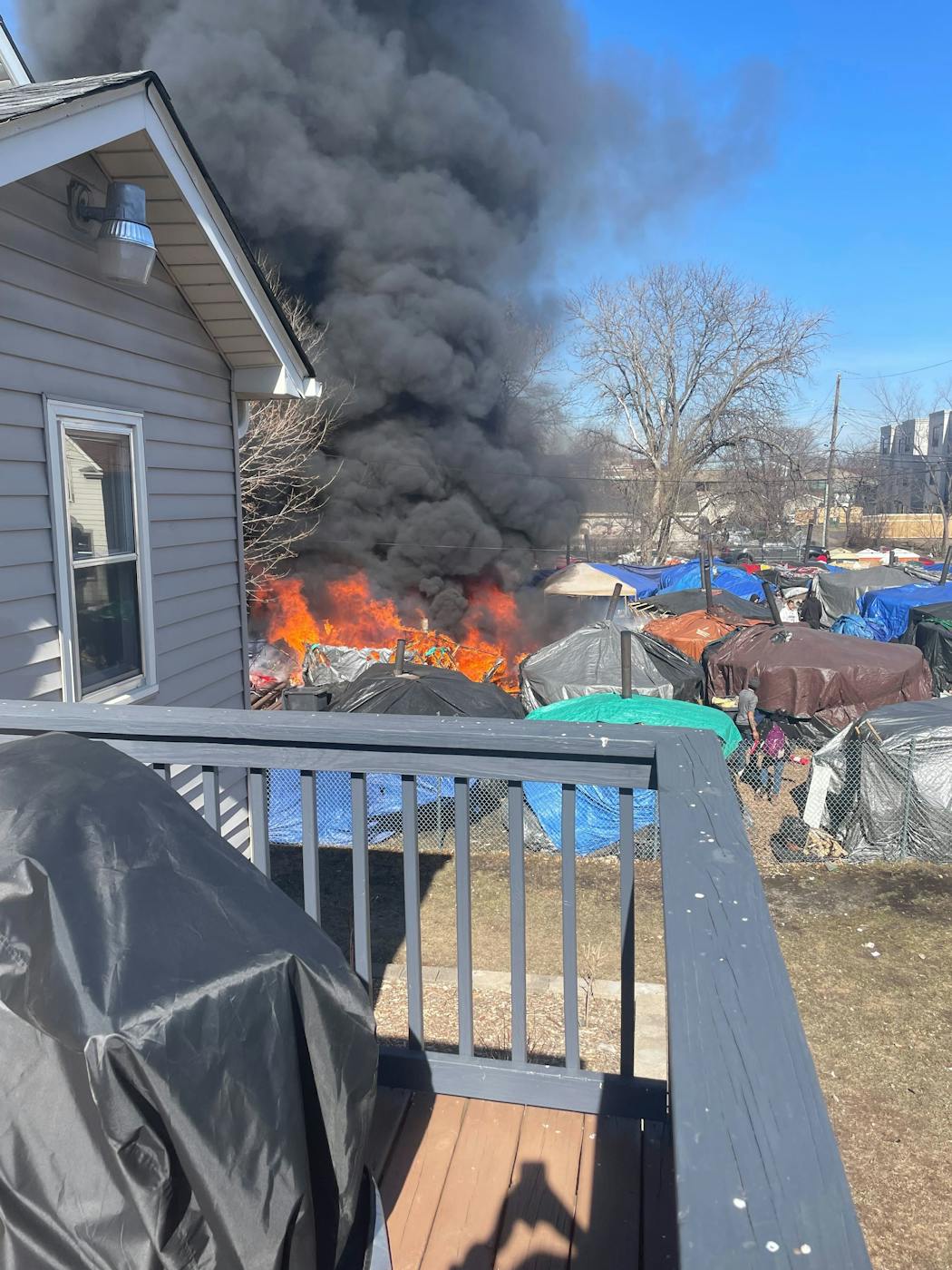Large flames and smoke are visible from an encampment in the 1100 block of E. 28th Street, as seen from neighbor Ashley Jensen's home.