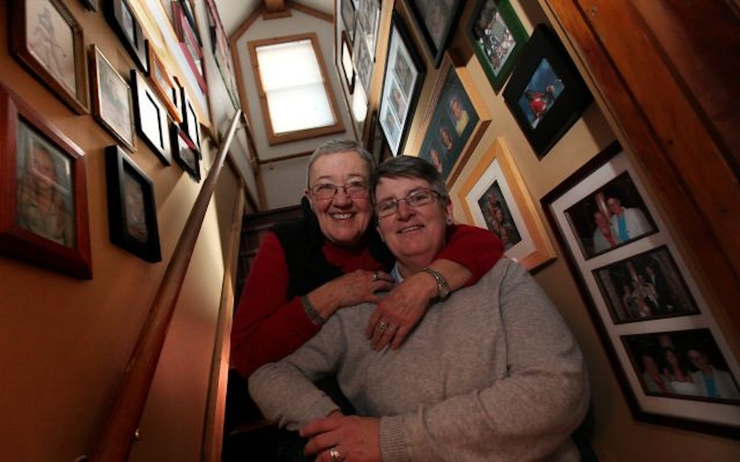 Nancy Edwards and Barbara Bradford sit on the stairs amongst the kids and grandchildren photos in their Minneapolis home.