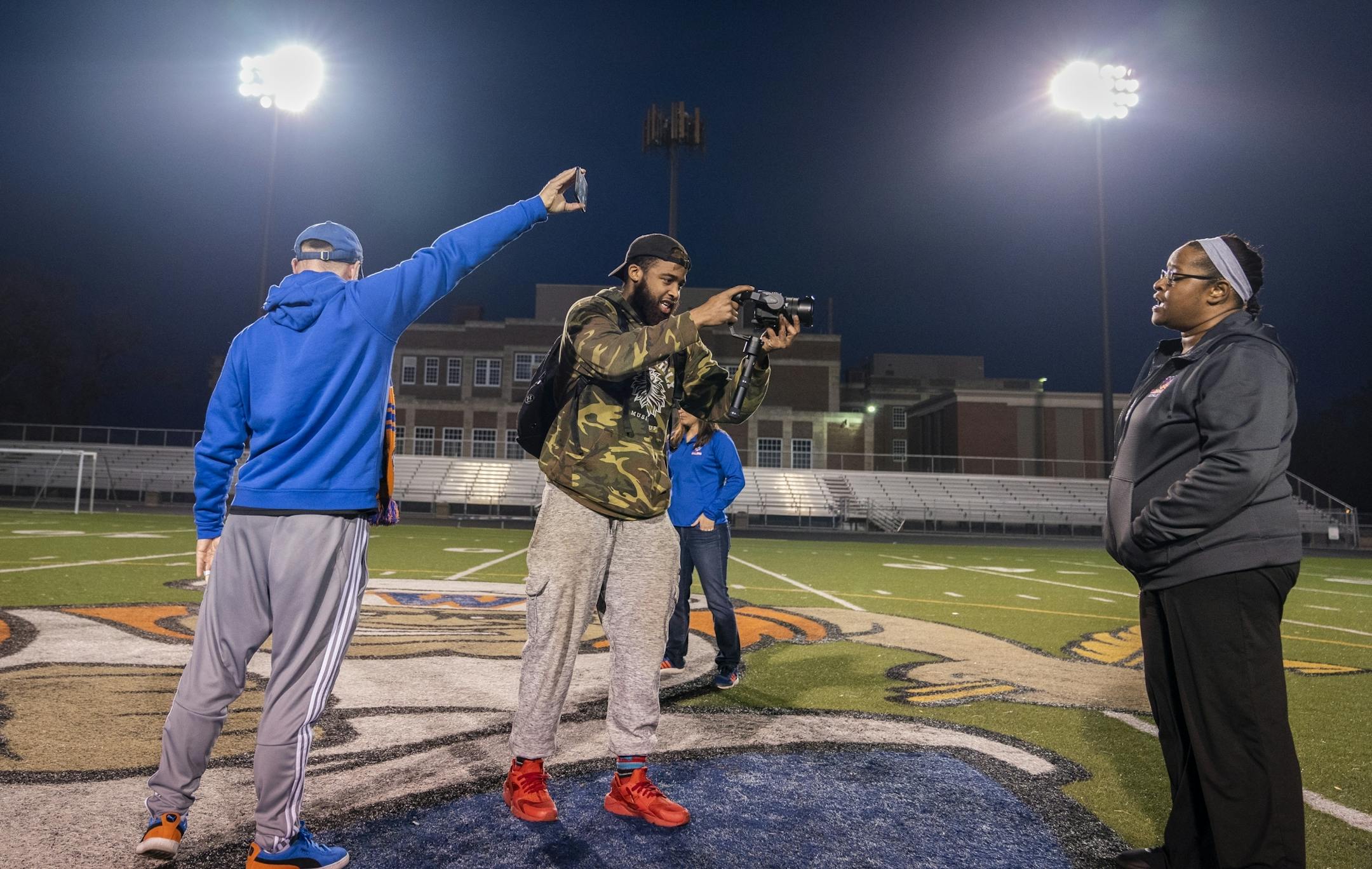 Charles Smith, center, associate educator/media support at Washburn, filmed assistant principal Shannon Tenner, right, conveying a message to the class of 2020 during the "Be The Light Minnesota" event as they turned on the stadium lights at Washburn High School for 20 minutes and 20 seconds for the class of 2020.