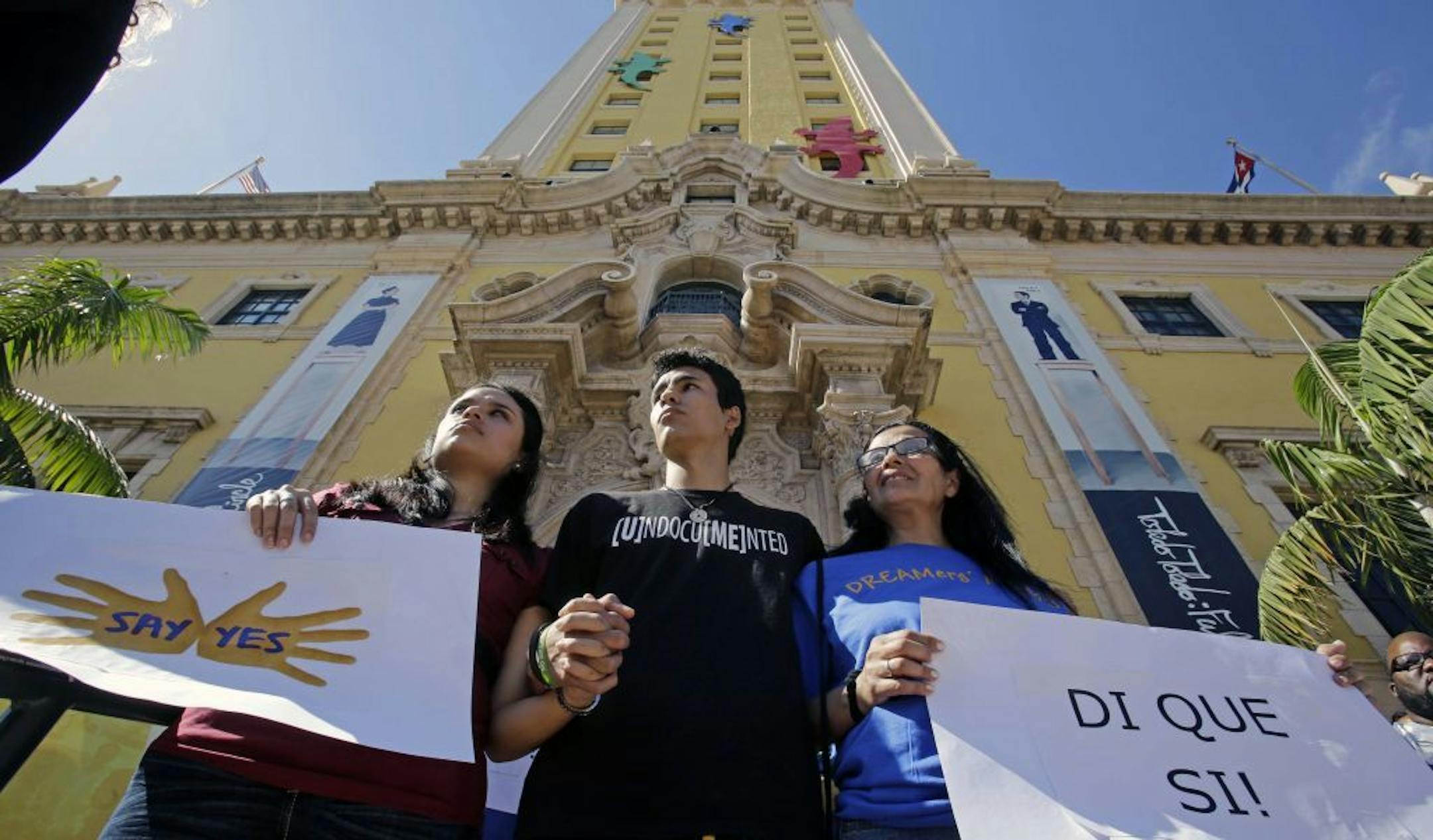 Federico Paseiro, center, his mother Patricia Sosa, right, both illegal immigrants of Argentina, and his girlfriend Daysis Moraga, an immigration activist, left, hold signs in front of the Freedom Tower in downtown Miami, Monday, Jan. 28, 2013. The Florida Immigrant Coalition, together with other immigrant families and community organizations have initiated the "Di Que Si!" campaign, which translates into English "Say yes!," demanding immigration reform that creates a system that keeps families