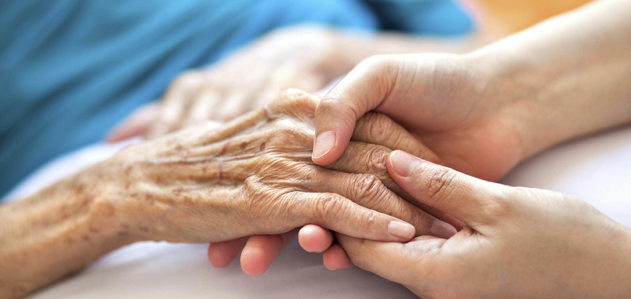 Woman holding senior woman's hand on bed