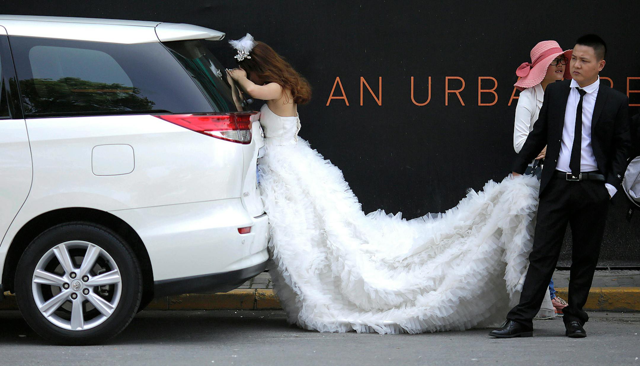 A newly wed bride rests in the shade as her groom helps holding the hem of her wedding dress during their wedding photo session in Shanghai, China, Friday, May 24, 2013.