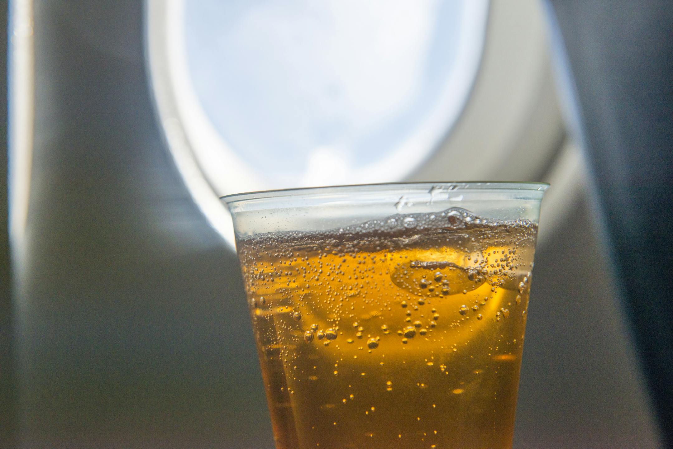 A drink of cider by an airplane window in flight.
