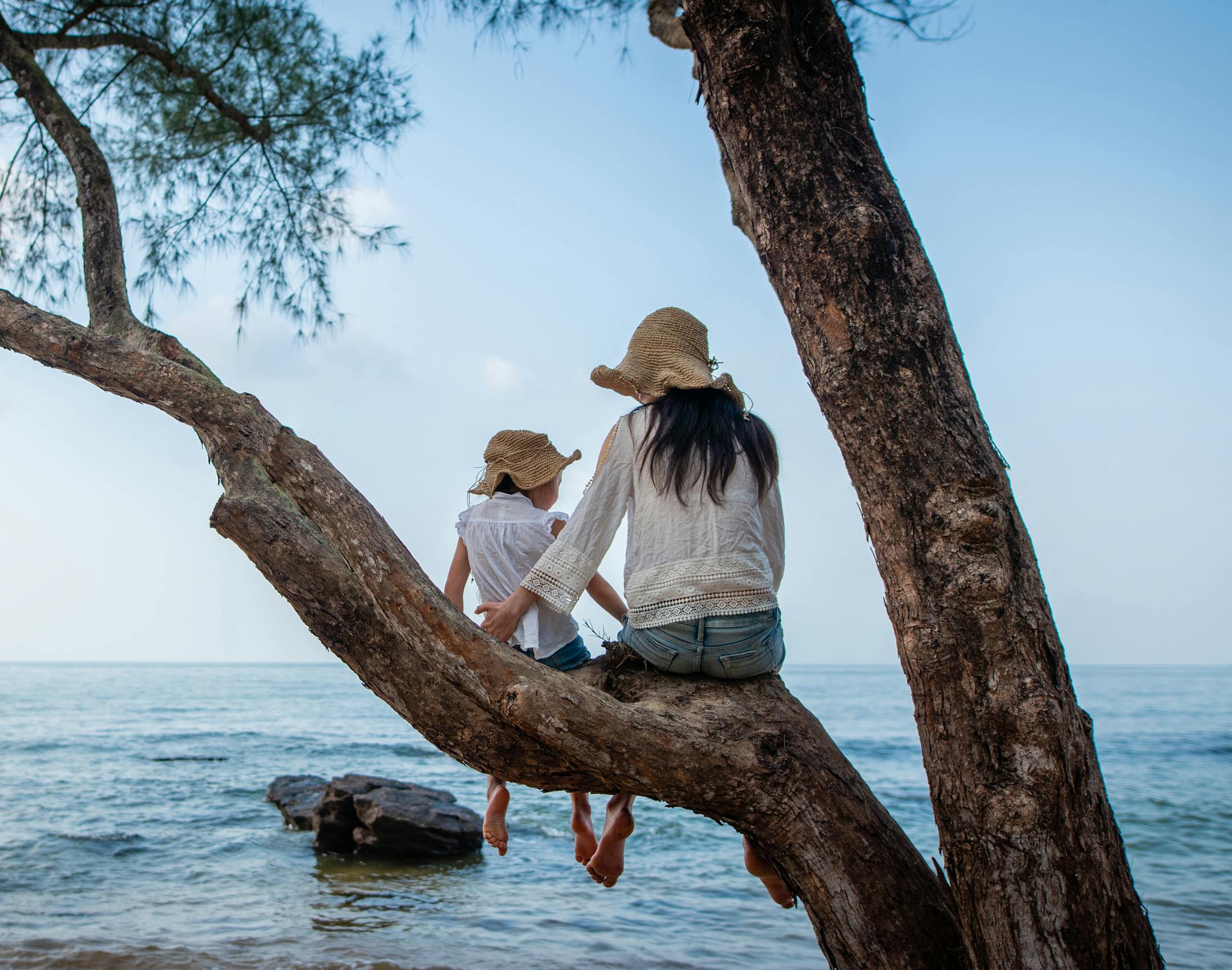 Mother and daughter sit on a tree at the beach