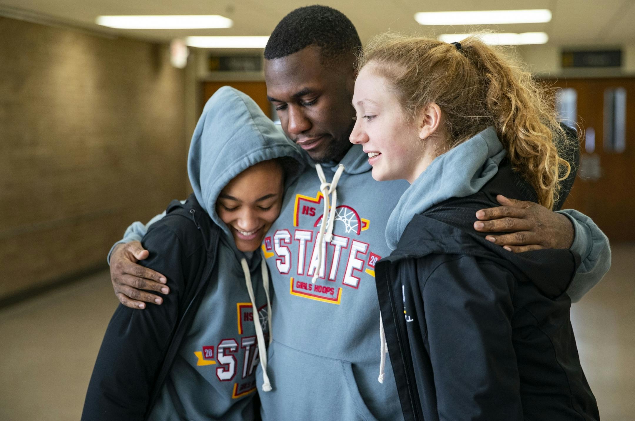 (Left) Duluth Marshall girl's basketball guards Grace Kirk and Gianna Kneepknes embraced head coach Chibuzo Osuchukwu in the lobby of the Marshall school on Friday after the MSHL girl's basketball tournament was cancelled.