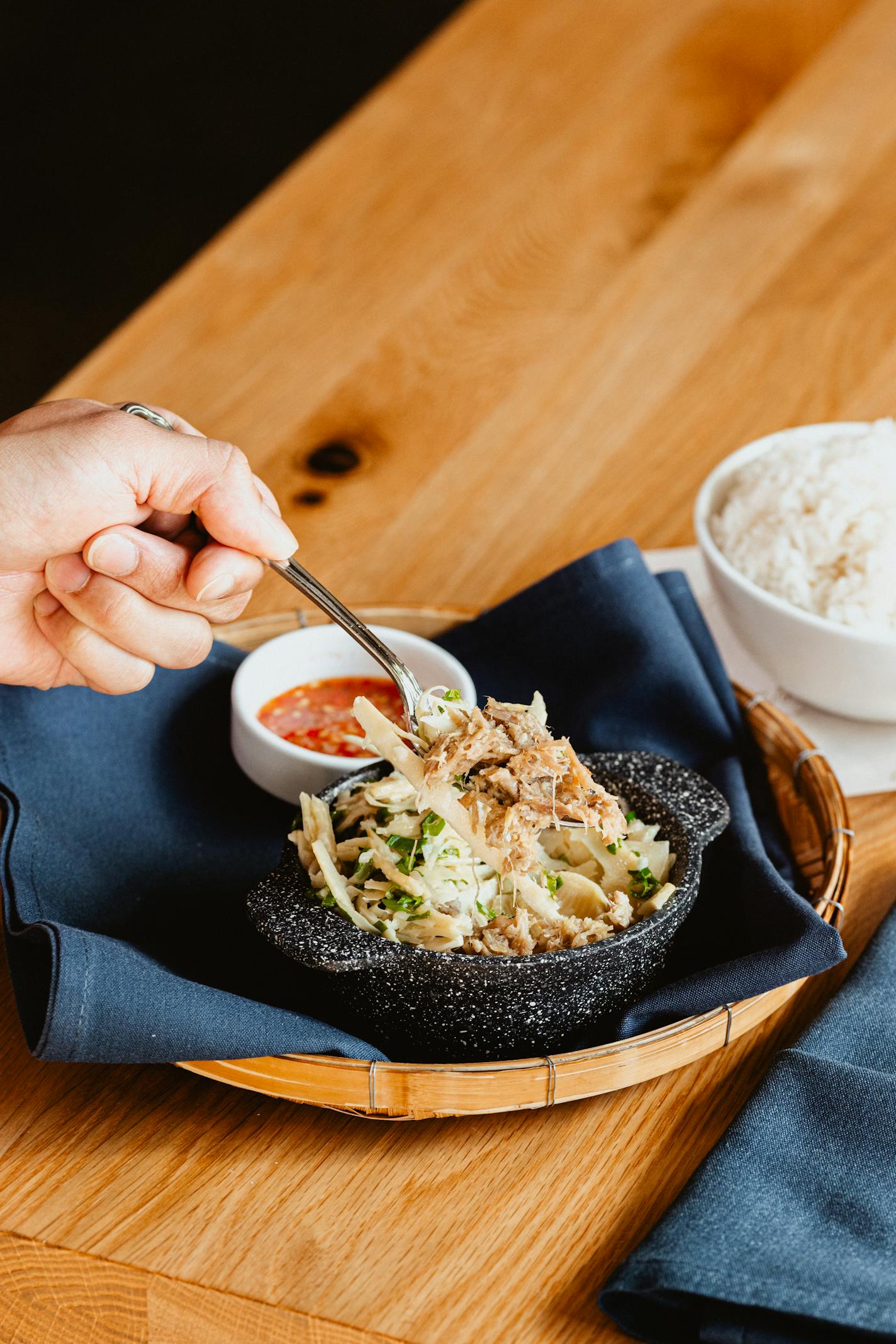 A hand scoops a small bowl of braised pork with a side of Diane's signature hot sauce.