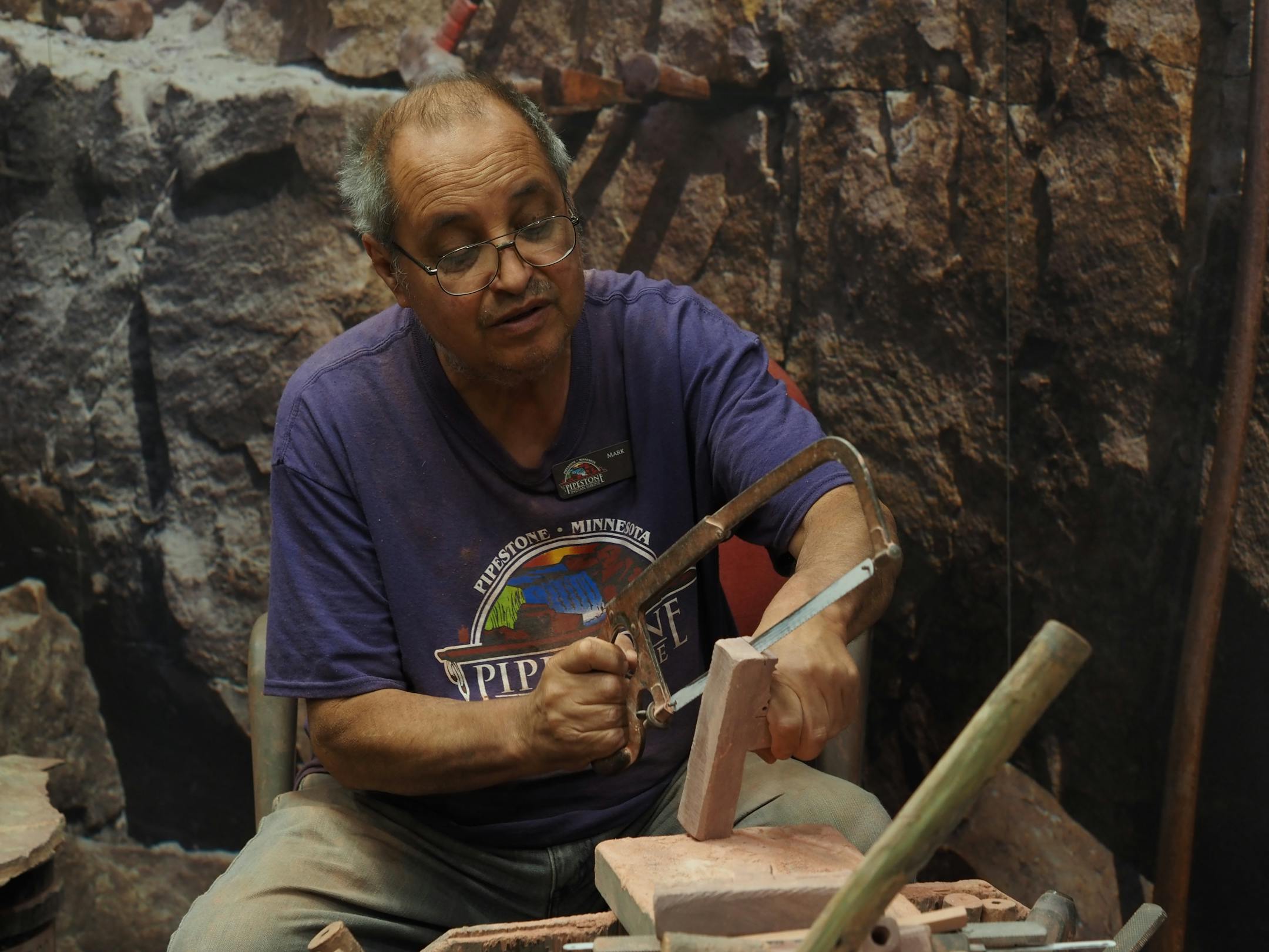 A demonstrator uses a hacksaw to shape a piece of pipestone at the Pipestone National Monument.