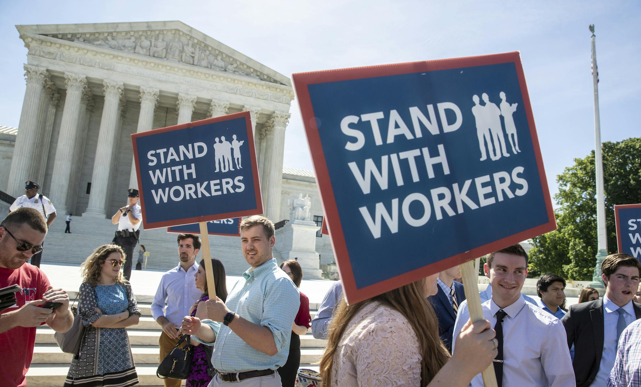 FILE - In this Monday, June 25, 2018 file photo, people gather at the Supreme Court awaiting a decision in an Illinois union dues case, Janus vs. AFSCME, in Washington. An Oregon state employee and a labor union have reached a settlement over her lawsuit seeking payback of obligatory union fees, marking the first refund of forced fees since the U.S. Supreme Court ruled in late June that government workers can't be required to contribute to labor groups, the employee's lawyers said Monday, July 3
