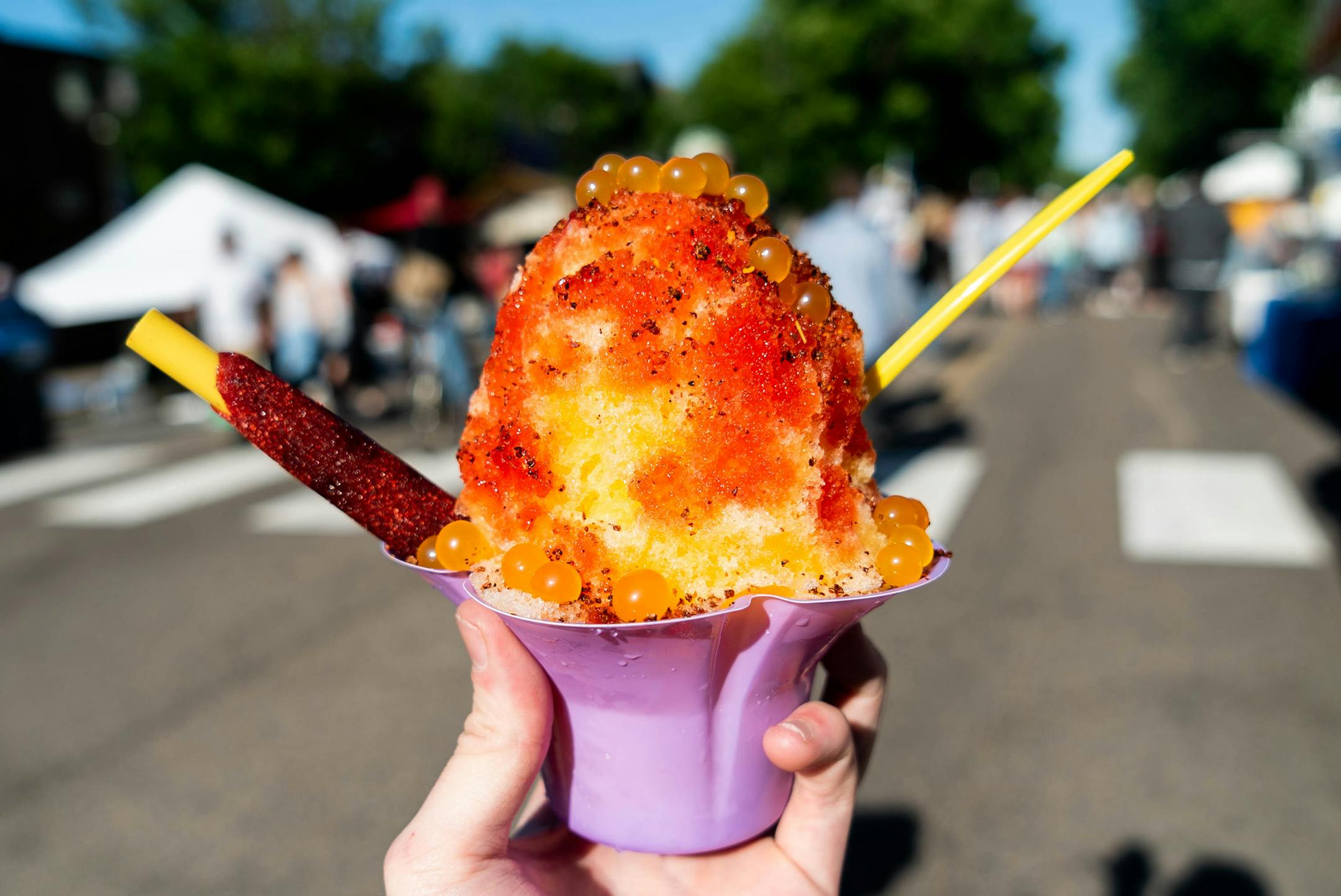 Mangonada Shave Ice: Mango-flavored shave ice drizzled with Mexican chamoy sauce, dusted with tajin chili powder, topped with popping mango boba pearls and served with a tamarind candy straw. At Minnesnowii Shave Ice, located in the south section of the West End Market.