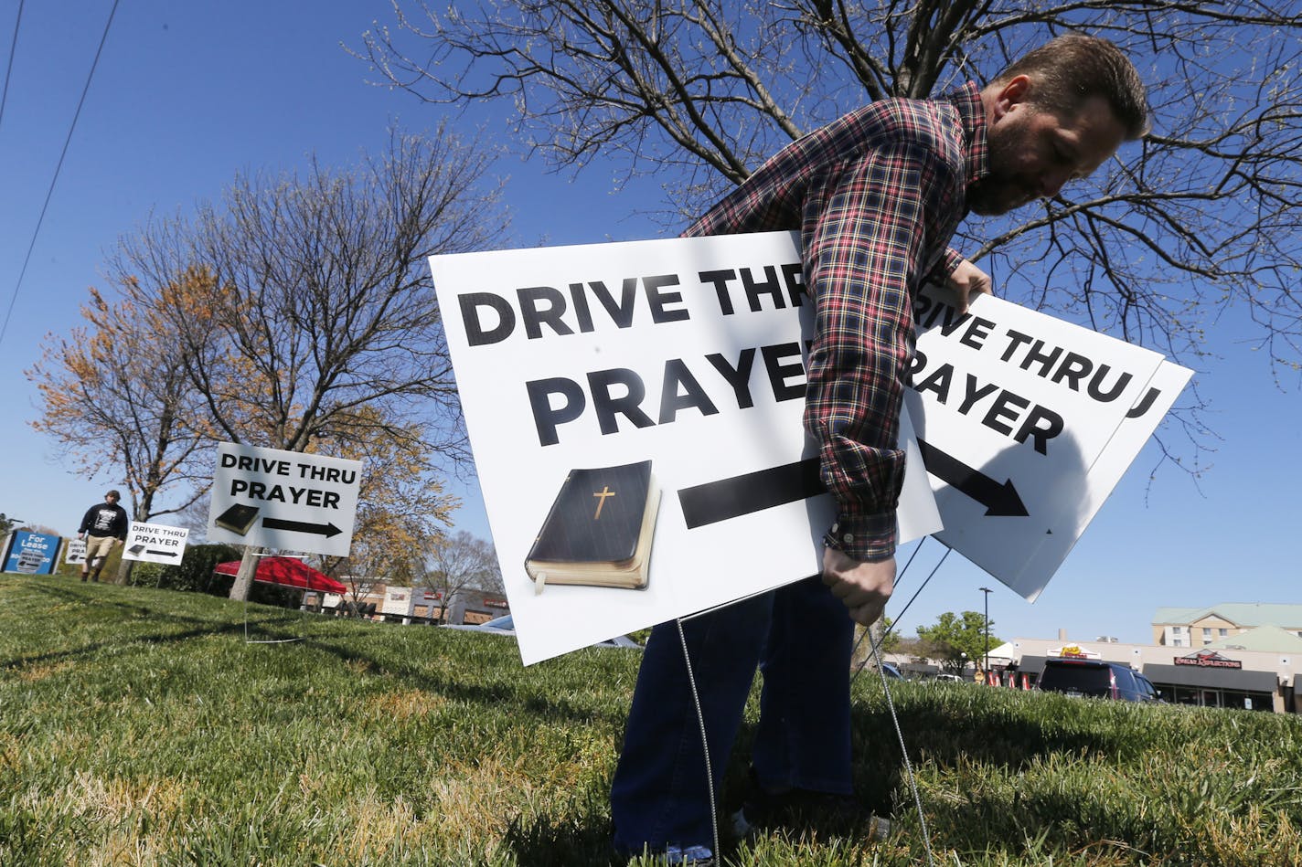 George DeCola, of Richmond, Va., places Drive Thru Prayer signs at a shopping center Thursday April 2, 2020, in Richmond, Va. DeCola, who is a worship leader at a Lutheran Church offers prayers for those wanting spiritual guidance. (AP Photo/Steve Helber)