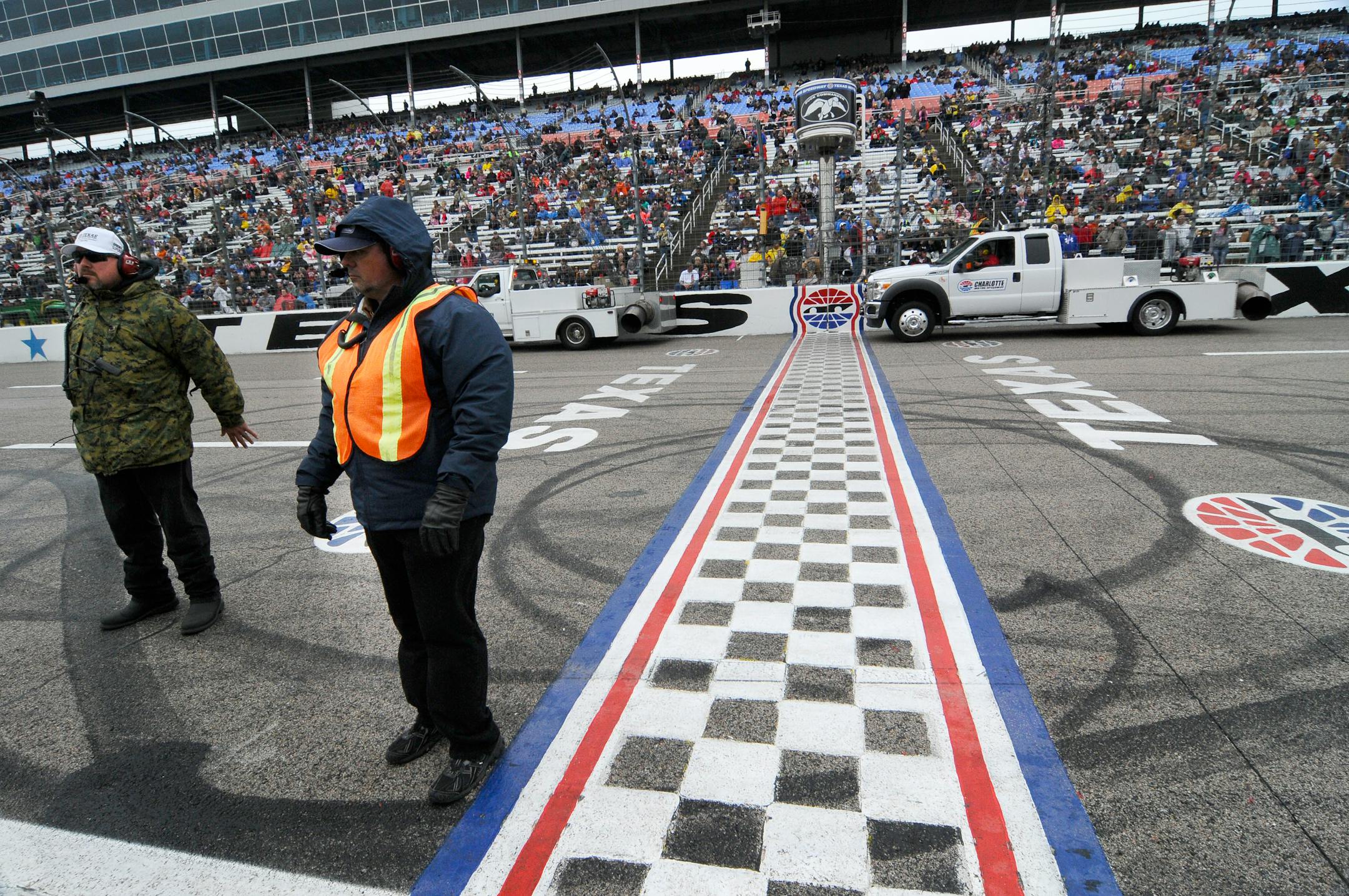 Track security guards Patrick Reyes, left, and Richard Gyure stood by the start-finish line as blowers worked on the track during Sunday's rain delay at Texas Motor Speedway. The race will be run Monday.