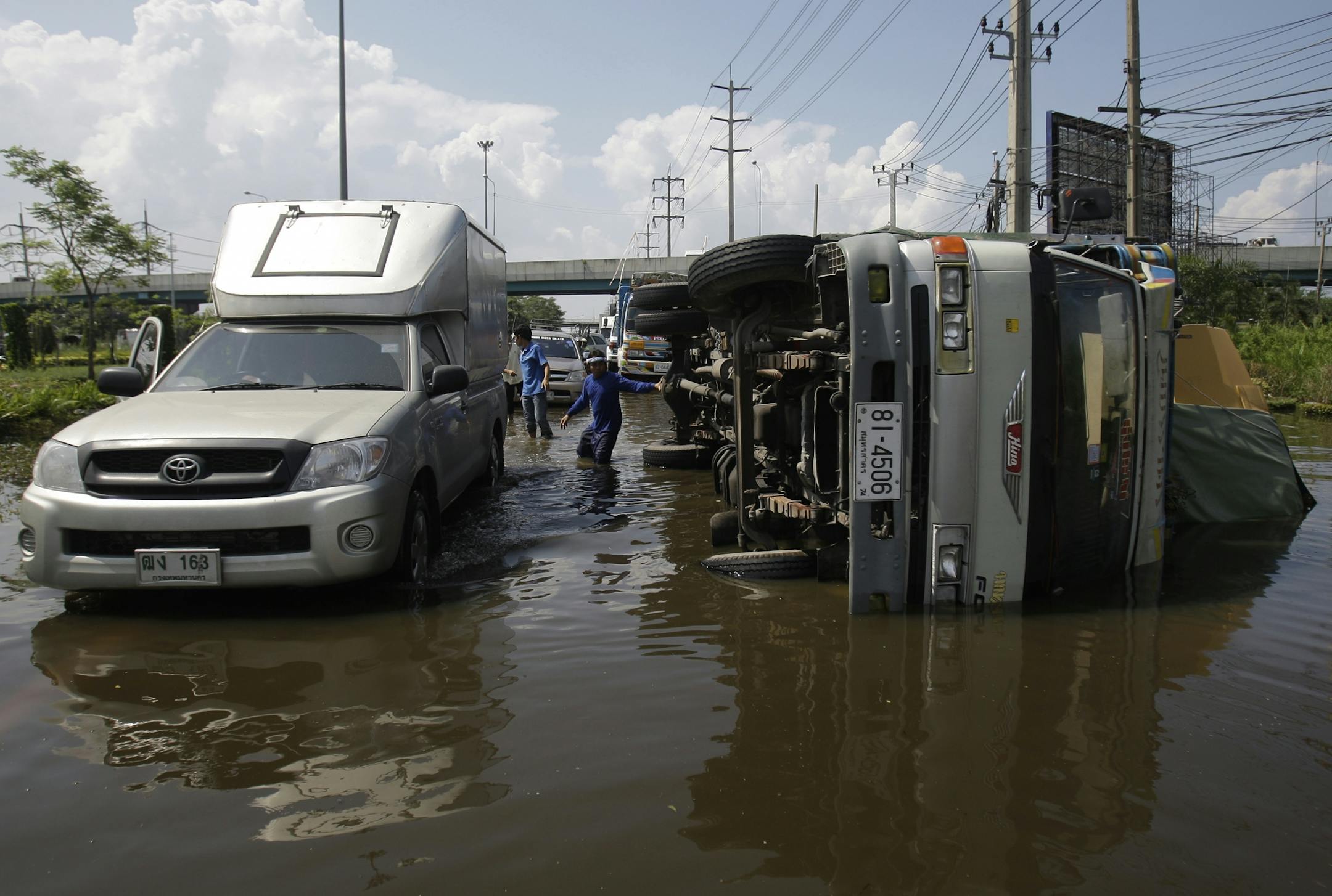A Thai man stands close to a truck that lies on its side after it fell on a big hole along a flooded road at Lat Krabang district in Bangkok, Thailand, Monday, Nov. 7, 2011. Thailand's record high floods continue to creep closer to the heart of the capital.