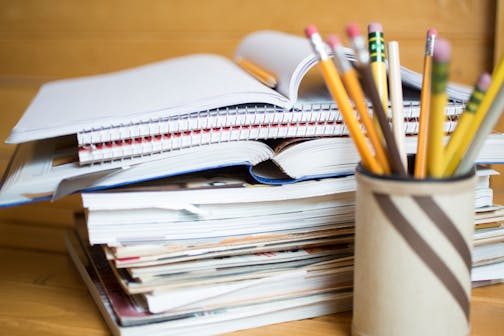 Stack of school books and pencil holder on desk.