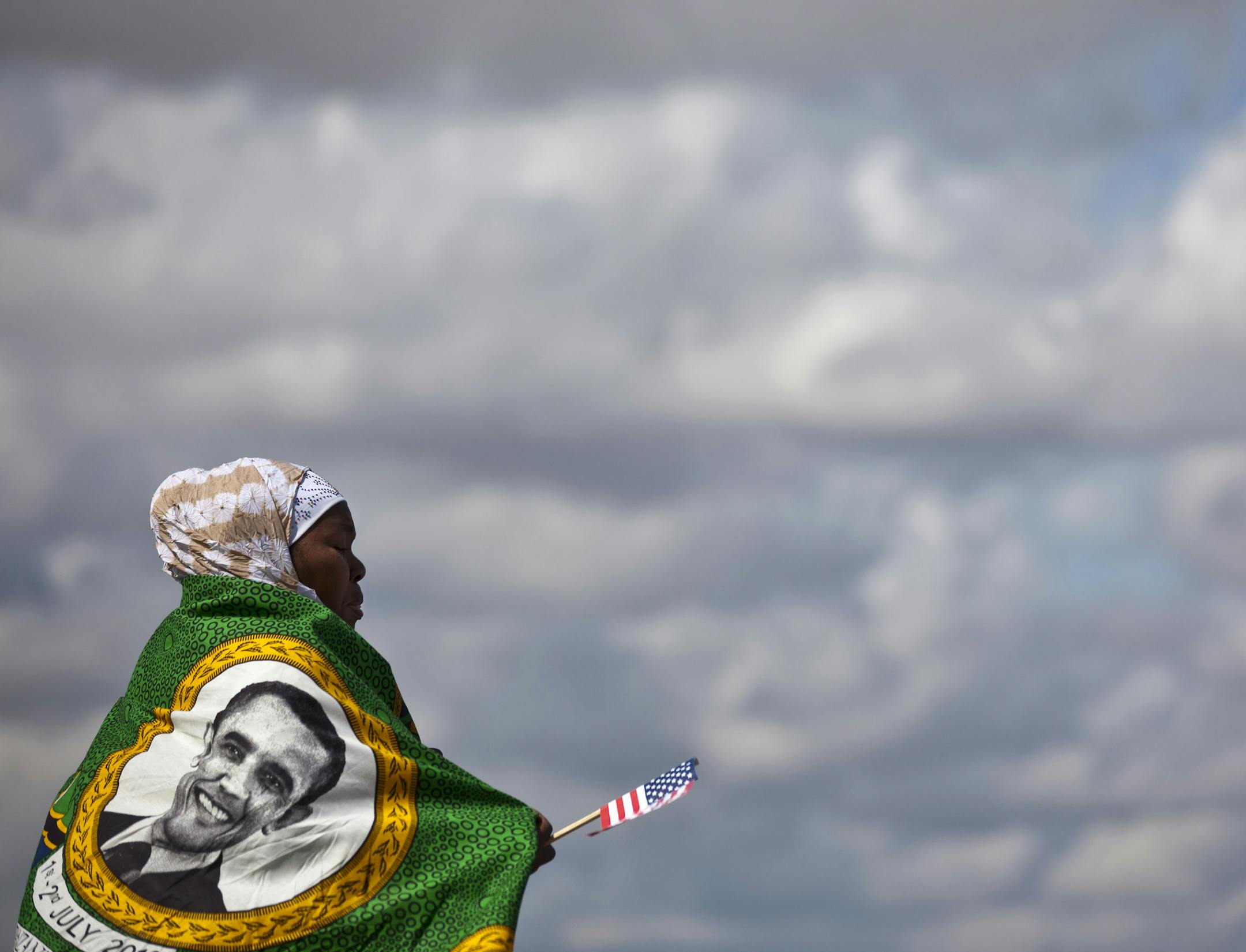 In this photo taken Tuesday July 2, 2013, A woman from a welcoming group wears a shawl with the face of U.S. President Barack Obama, as she prepares for him to depart from the Julius Nyerere airport at the end of the final leg of his weeklong visit to Africa, in Dar es Salaam, Tanzania. Barack Obama, the United States’ first African-American president, has captured the imagination of people across the continent where his face shows up on billboards, backpacks, T-shirts and restaurants. On