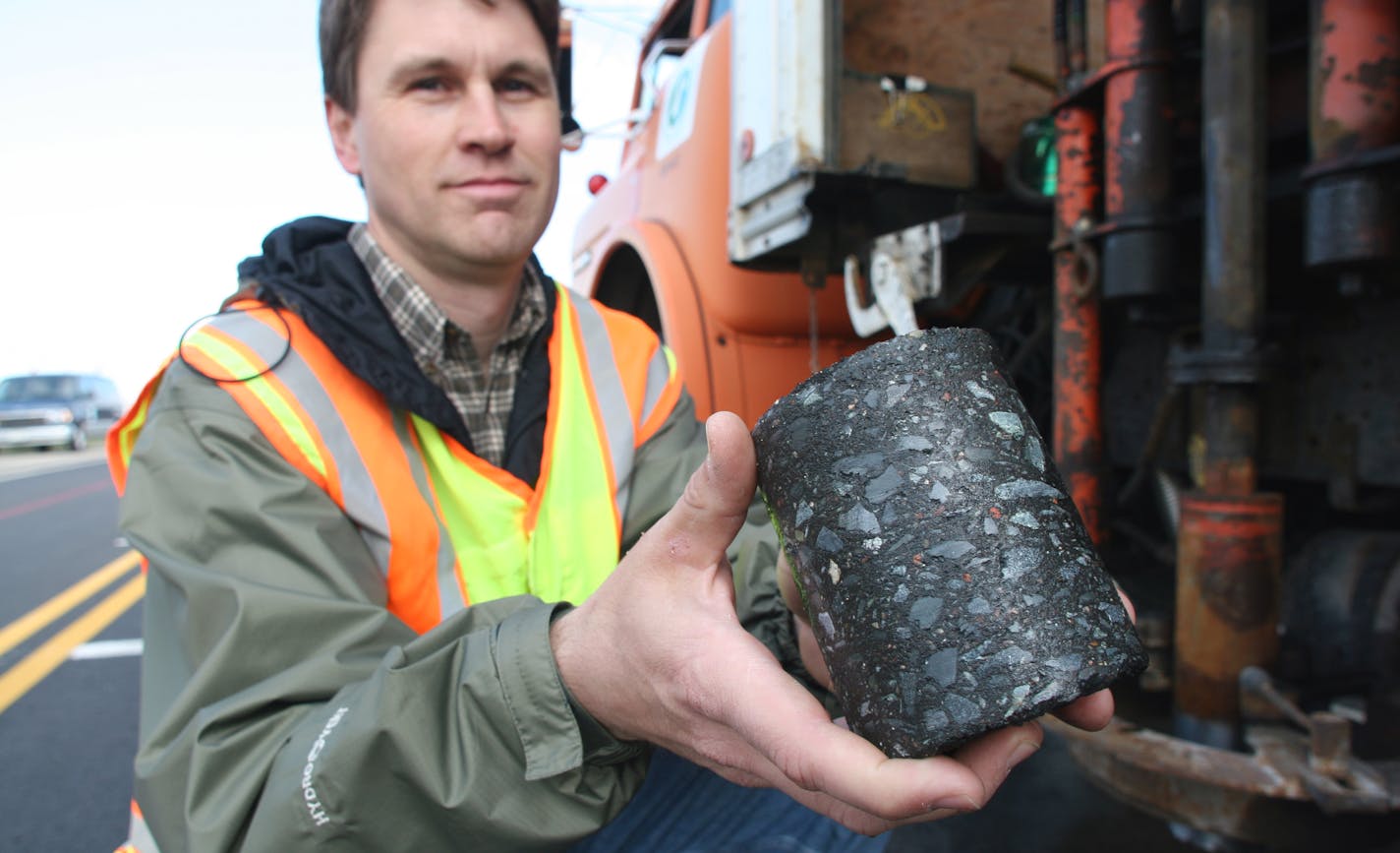 MnRoad operations engineer Ben Worel holds a core taken from an asphalt road. The coring bit, mounted on a truck, is beside him.