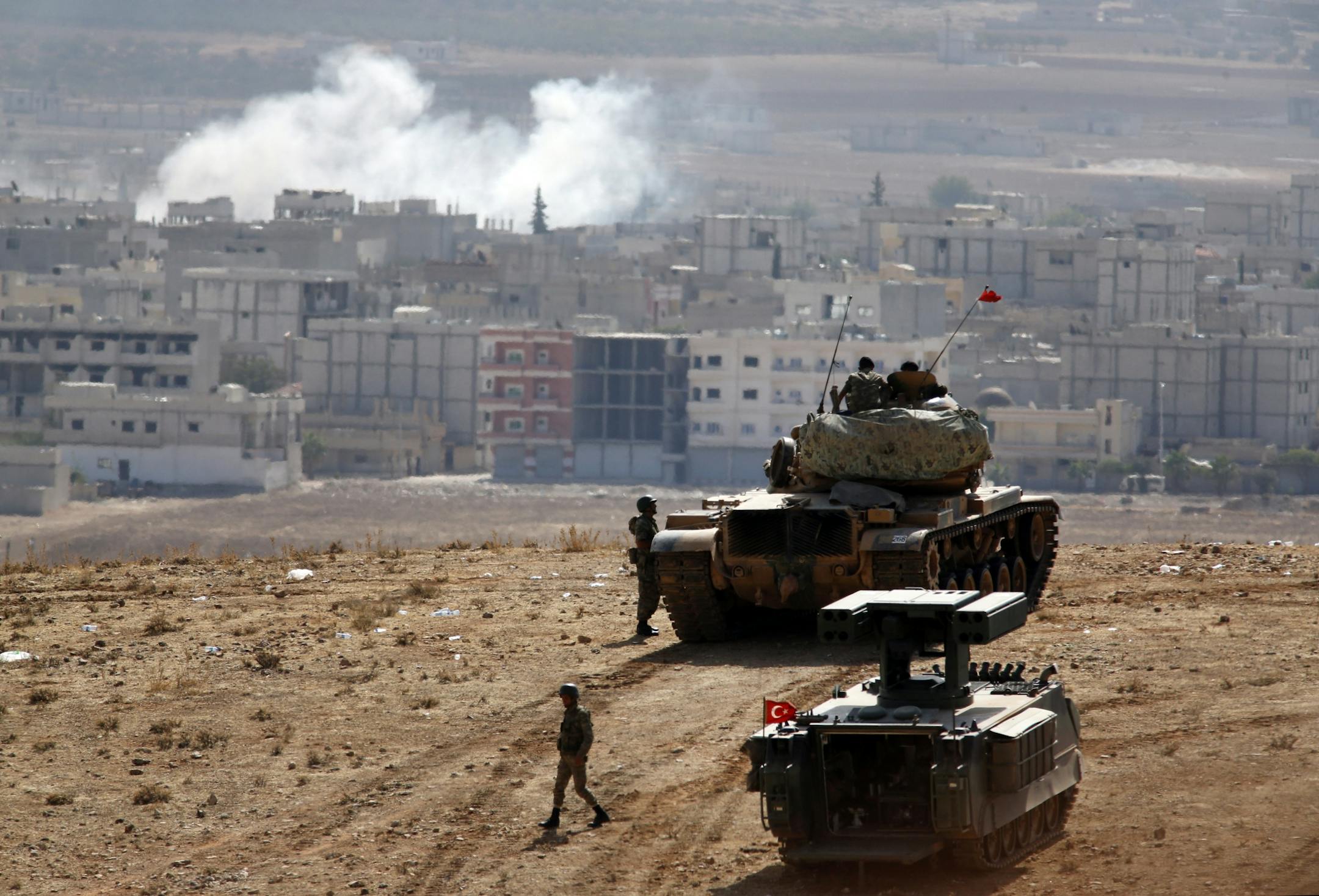 Turkish soldiers stand with a tank and an armoured vehicle as they hold their positions on a hilltop in the outskirts of Suruc, Turkey, at the Turkey-Syria border, overlooking smoke rising from a strike in Kobani, Syria, during fighting between Syrian Kurds and the militants of Islamic State group, Thursday, Oct. 9, 2014. Kobani, also known as Ayn Arab, and its surrounding areas, has been under assault by extremists of the Islamic State group since mid-September and is being defended by Kurdish