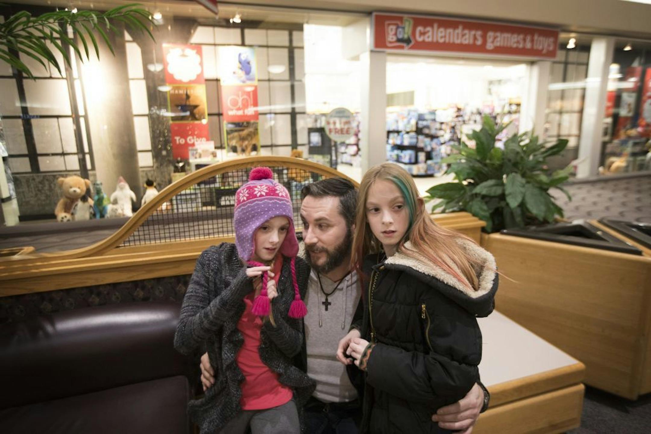 Isabelle, left, and Abby Carlsen listen as their father, Jesse, tells them a secret while shopping Kirkland Mall in Bismarck.