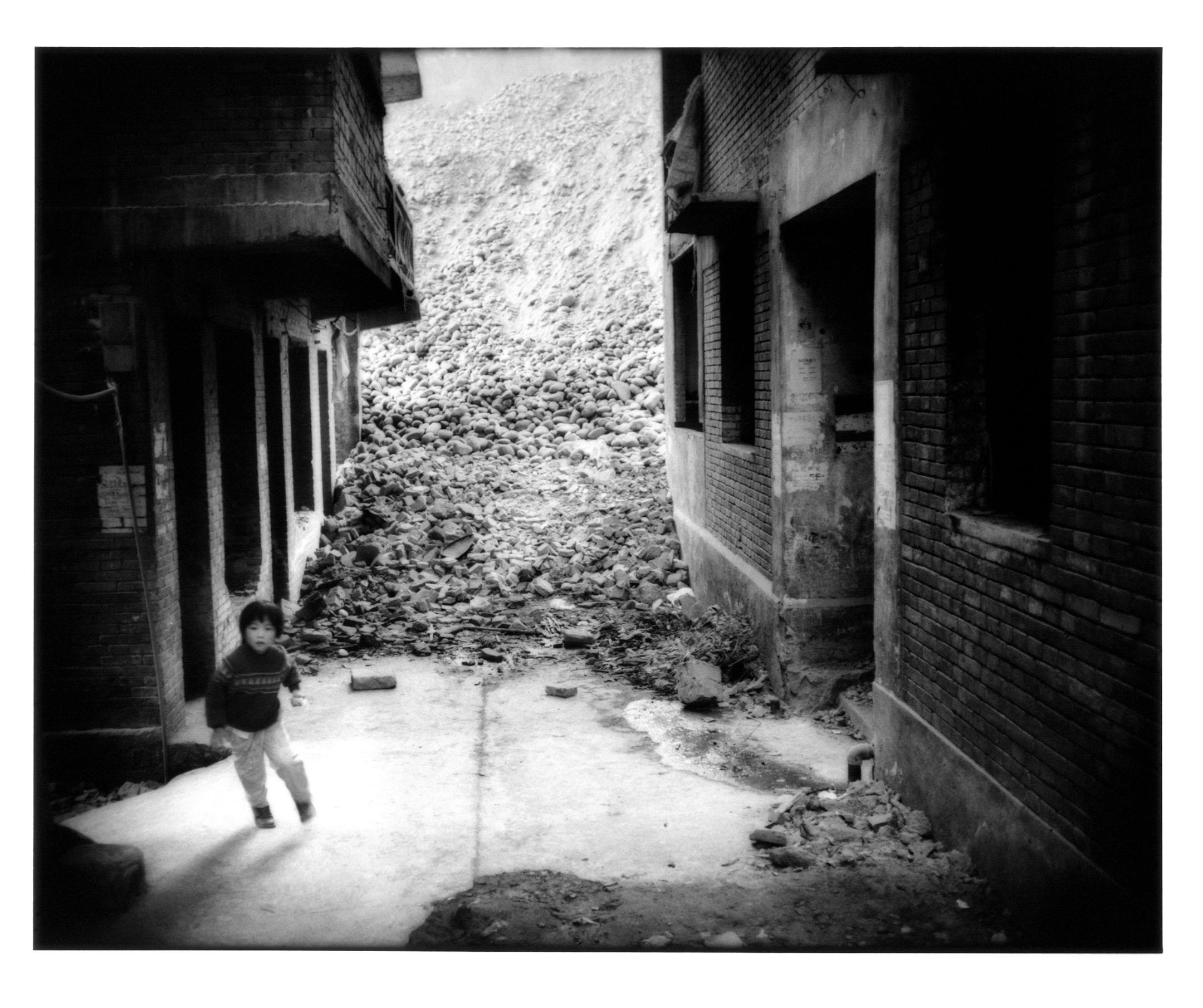 Boy playing amidst demolition rubble flows into alleyway where the last remaining residents of Fengdu still live. Most of the building are unoccupied and gutted. Three Gorges of the Yangtze