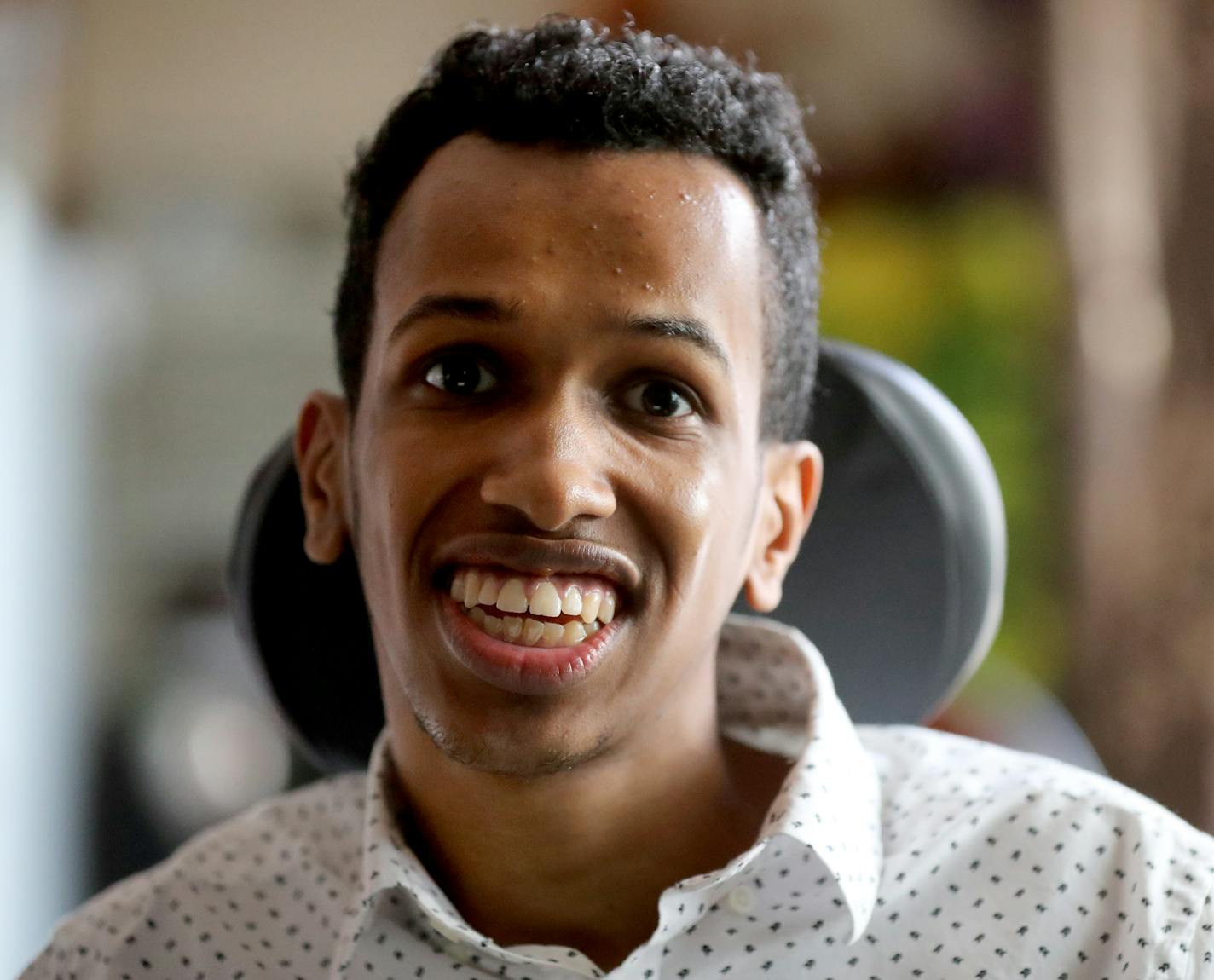 Ahmed Ali, 21, seen in his motorized chair, hung out with his siblings Abdullahi, 10, and Raqiya, 8, not seen, where Ahmed quizzed them, using his computer as his voice and typing questions into it about things like their favorite colors, or movies or foods. "Education is a big part of his life," says his mother Hamdi. Ahmed was his school's valedictorian and his commencement speech using assistive technology went viral - marking the first time the district used assistive technology at a graduat