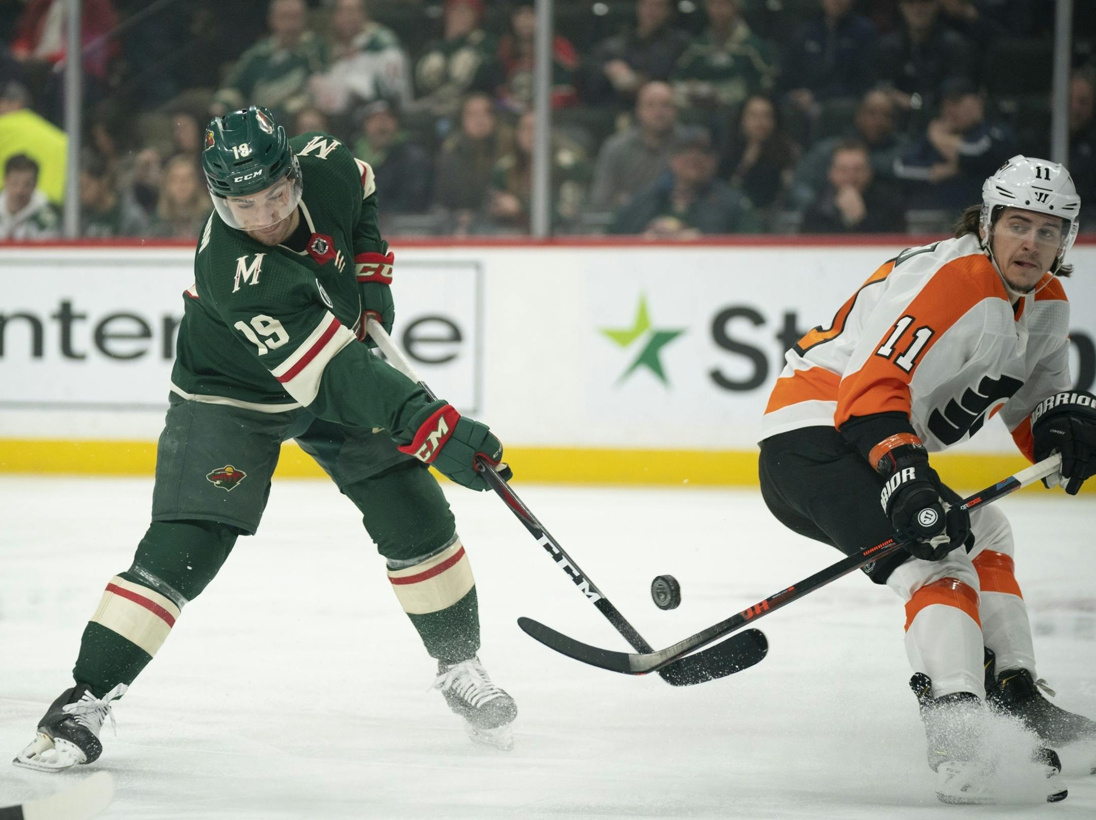 Minnesota Wild center Luke Kunin (19) slapped at a flying puck in front of the Flyers net while Philadelphia Flyers right wing Travis Konecny (11) defended.