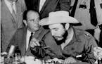 April 27, 1959 Eats Under Guard -- Cuba's Premier Fidel Castro, has a hurried meal under watchful eyes of Houston police after his arrival here today.