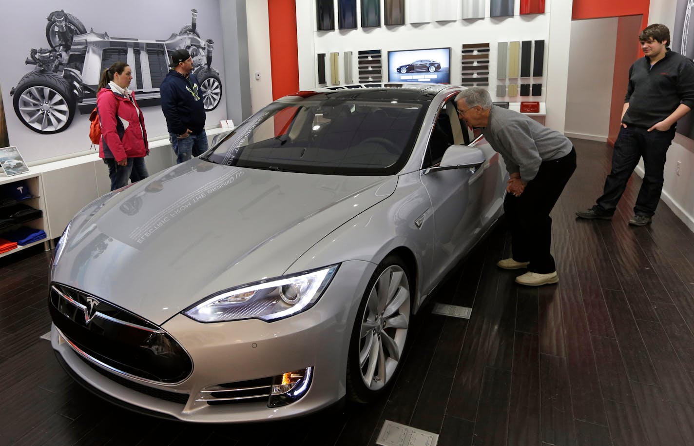 Tesla representative John Van Cleave, right, shows customers Sarah and Robert Reynolds, left, and Vince Giardina, a new Tesla all electric car, Monday, March 17, 2014, at a Tesla showroom inside the Kenwood Towne Centre in Cincinnati.